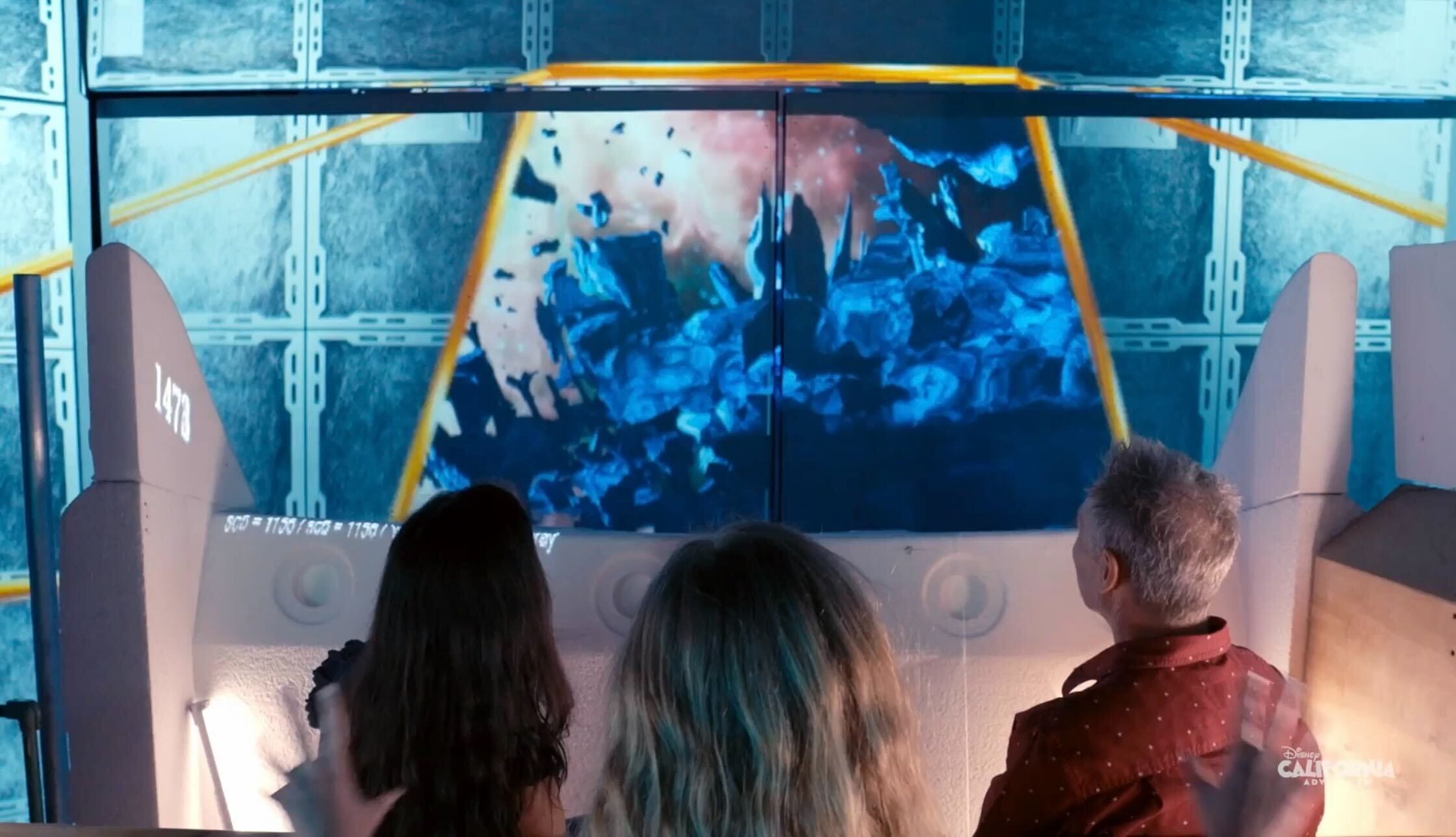 A group of people watch a large screen displaying an explosion scene in a futuristic setting, with debris flying and a bright background. The 3D experience immerses them in the chaos, reminiscent of an Avengers: Infinity Defense sequence.