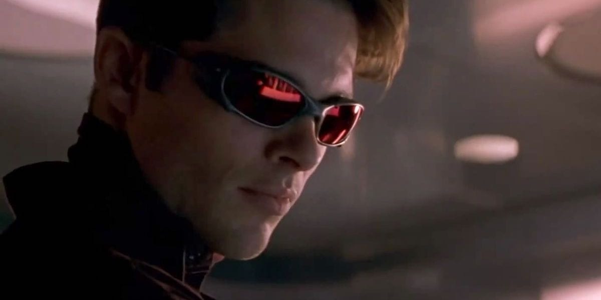 With a focused expression, the person in dark sunglasses looks down. Subtle reflections of red light dance across the lenses, reminiscent of something you'd see in a scene featuring James Marsden joining an intense moment on screen.