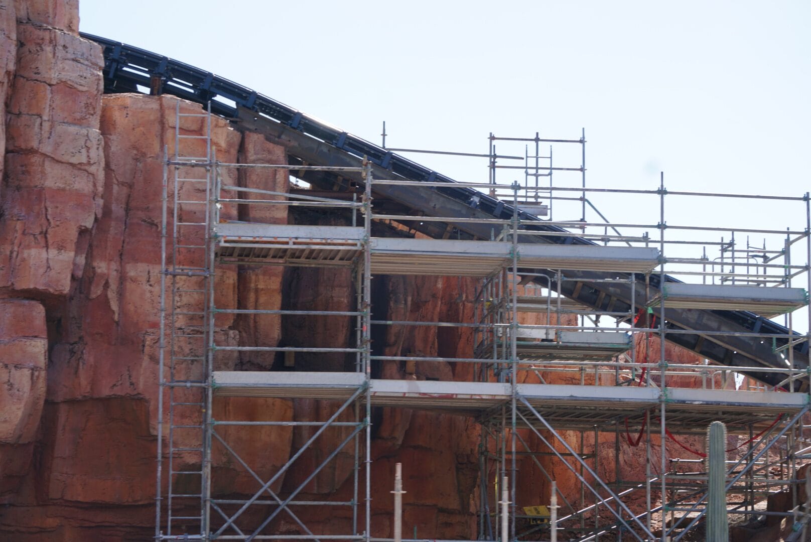 Scaffolding set up around a rocky facade with a partially constructed roller coaster track above resembles the early stages of Big Thunder Mountain Railroad's iconic lift hill at Magic Kingdom.