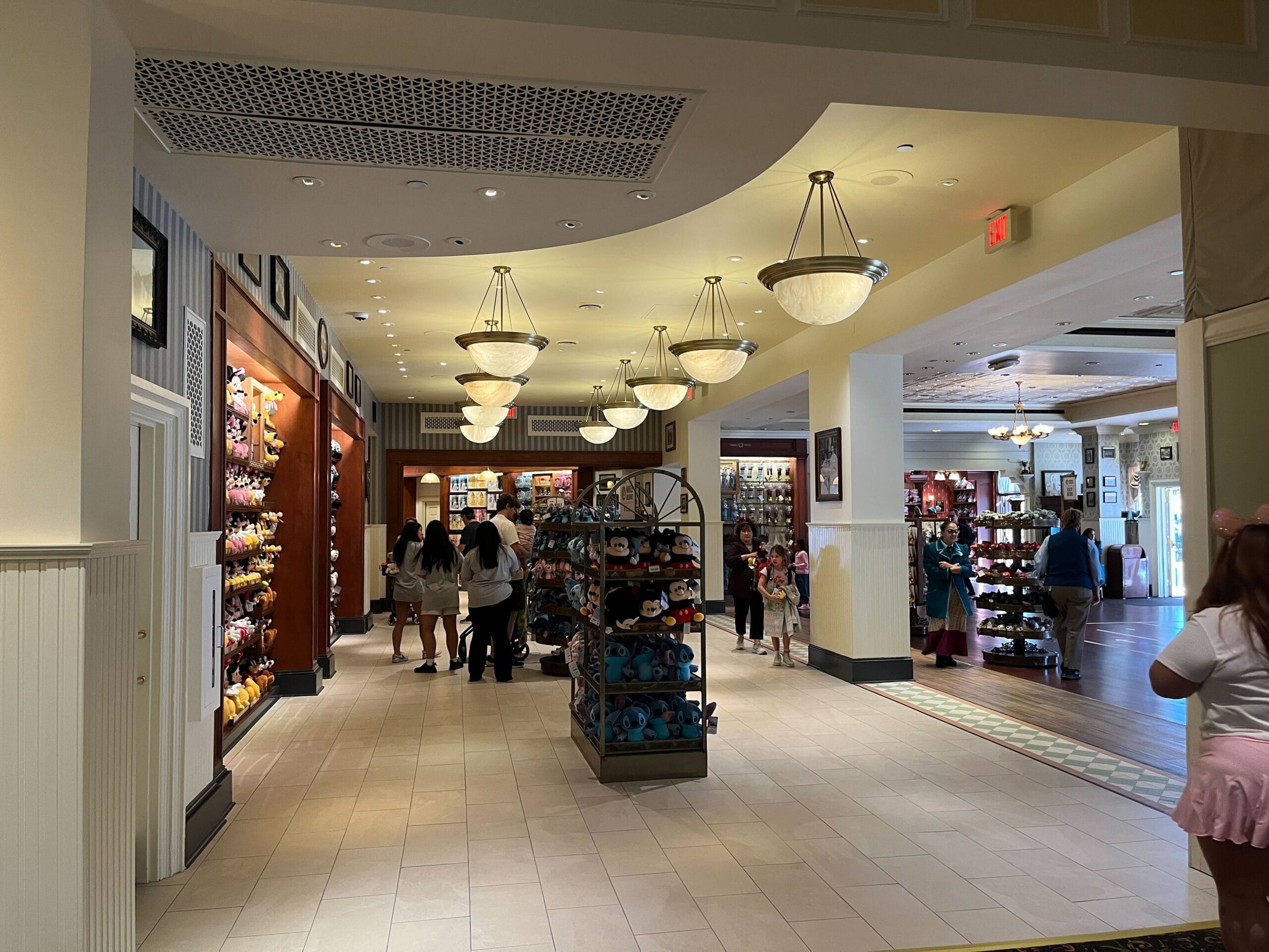 A retail store interior with shelves displaying merchandise. People are browsing products, and the ceiling is adorned with hanging lights. The floor is tiled in light colors.