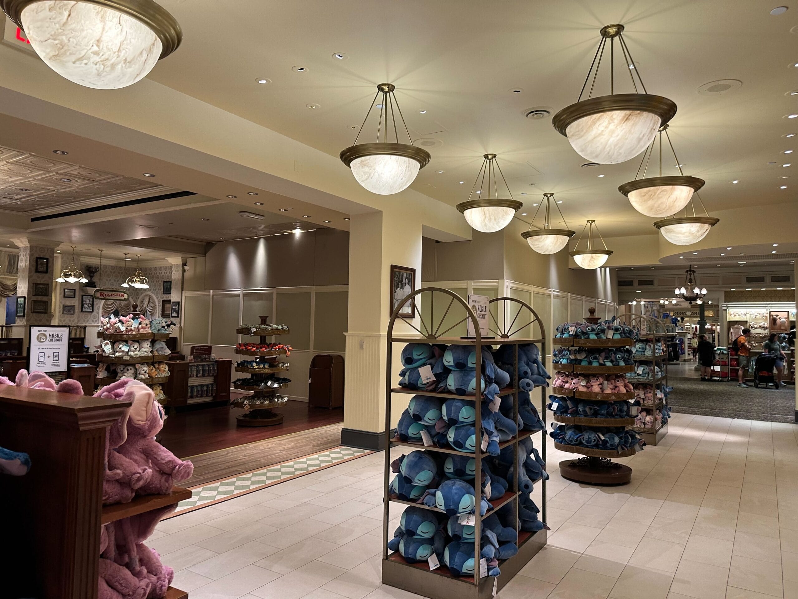 A well-lit store interior featuring shelves filled with plush toys and hats. The ceiling has multiple hanging dome lights, and there are various sections visible in the background.