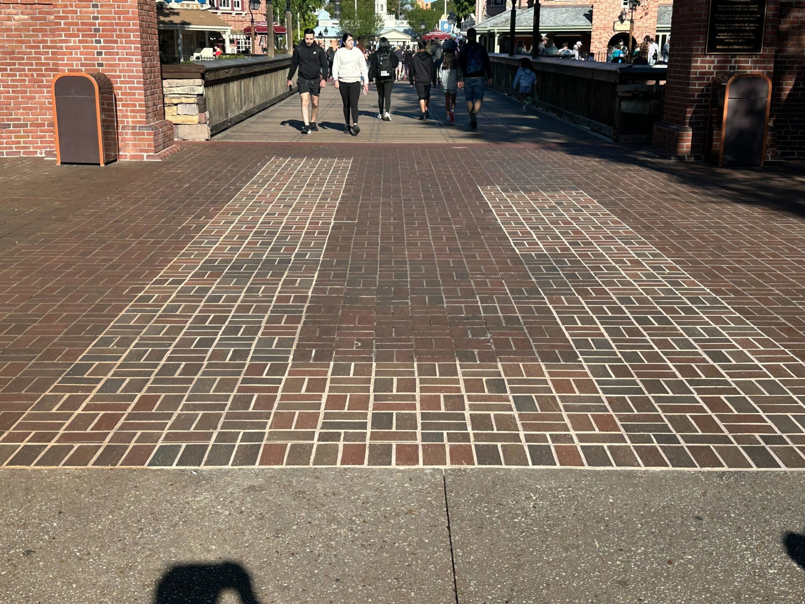 People walking on a brick path with a shadow of a person taking a photo.