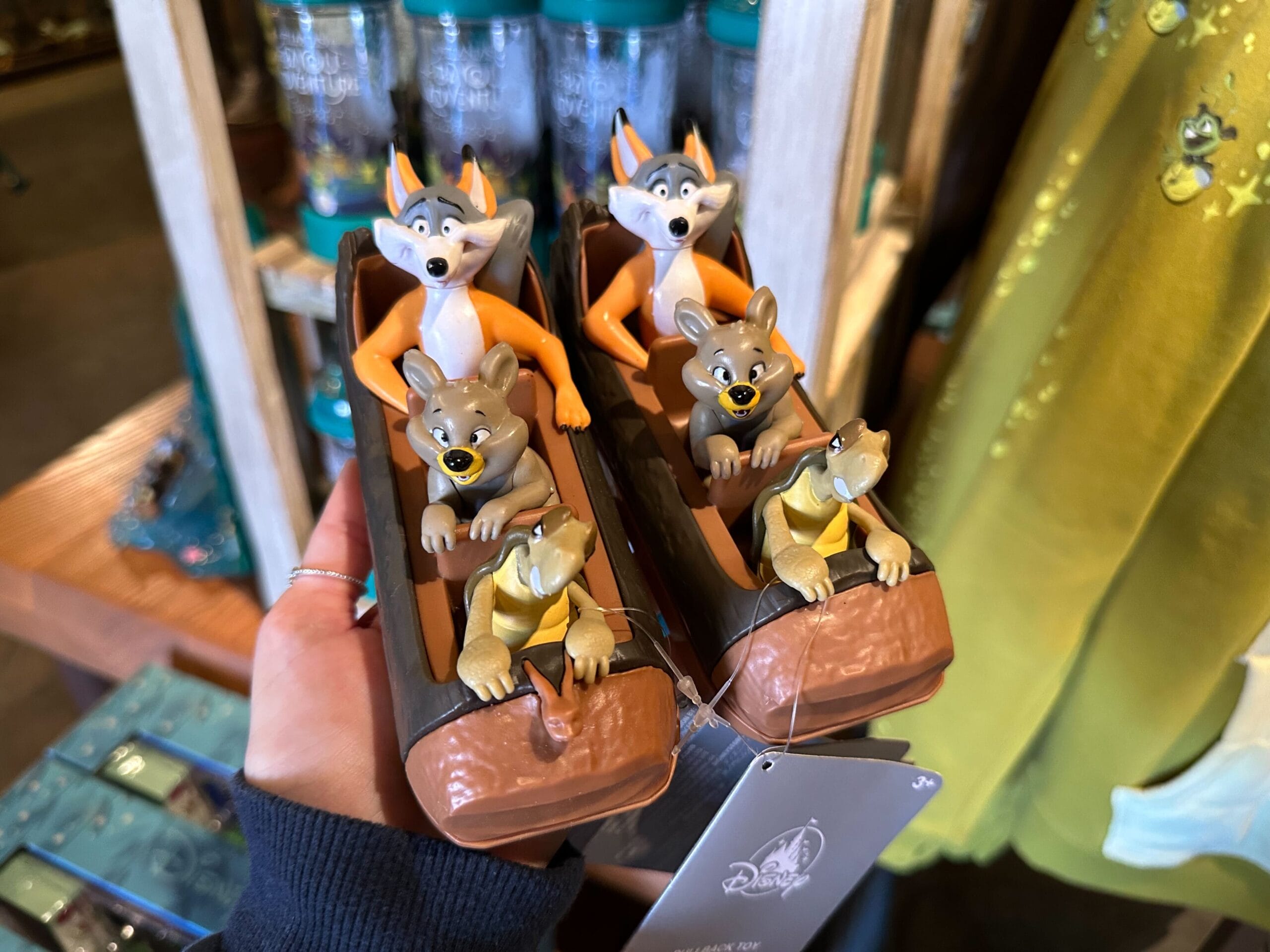 Figurines of cartoon animals, including a fox and a rabbit, riding in two brown log boats. Displayed in a store with various merchandise in the background.