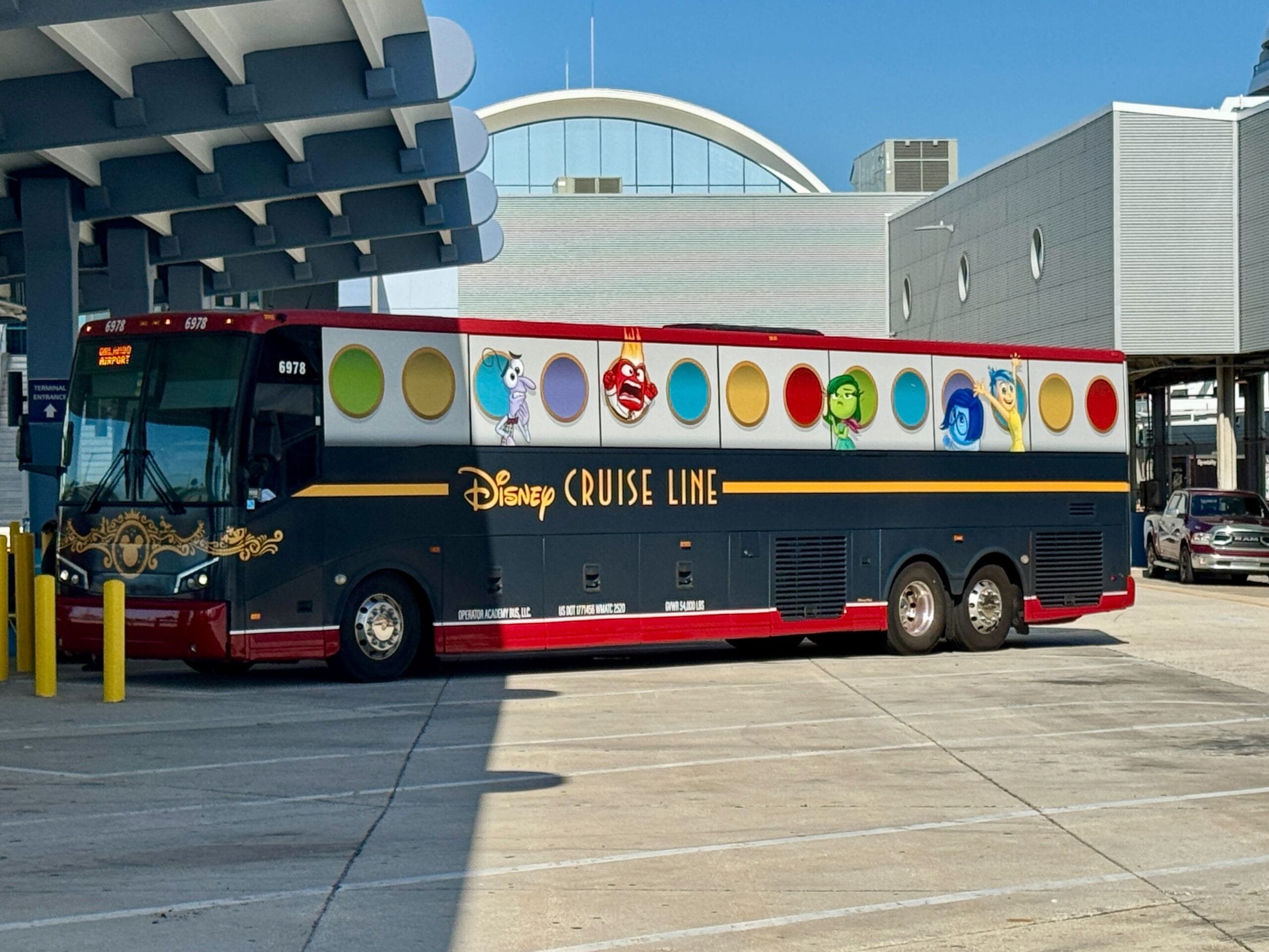 A Disney Cruise Line bus parked outside a terminal, featuring colorful Disney characters on its side.