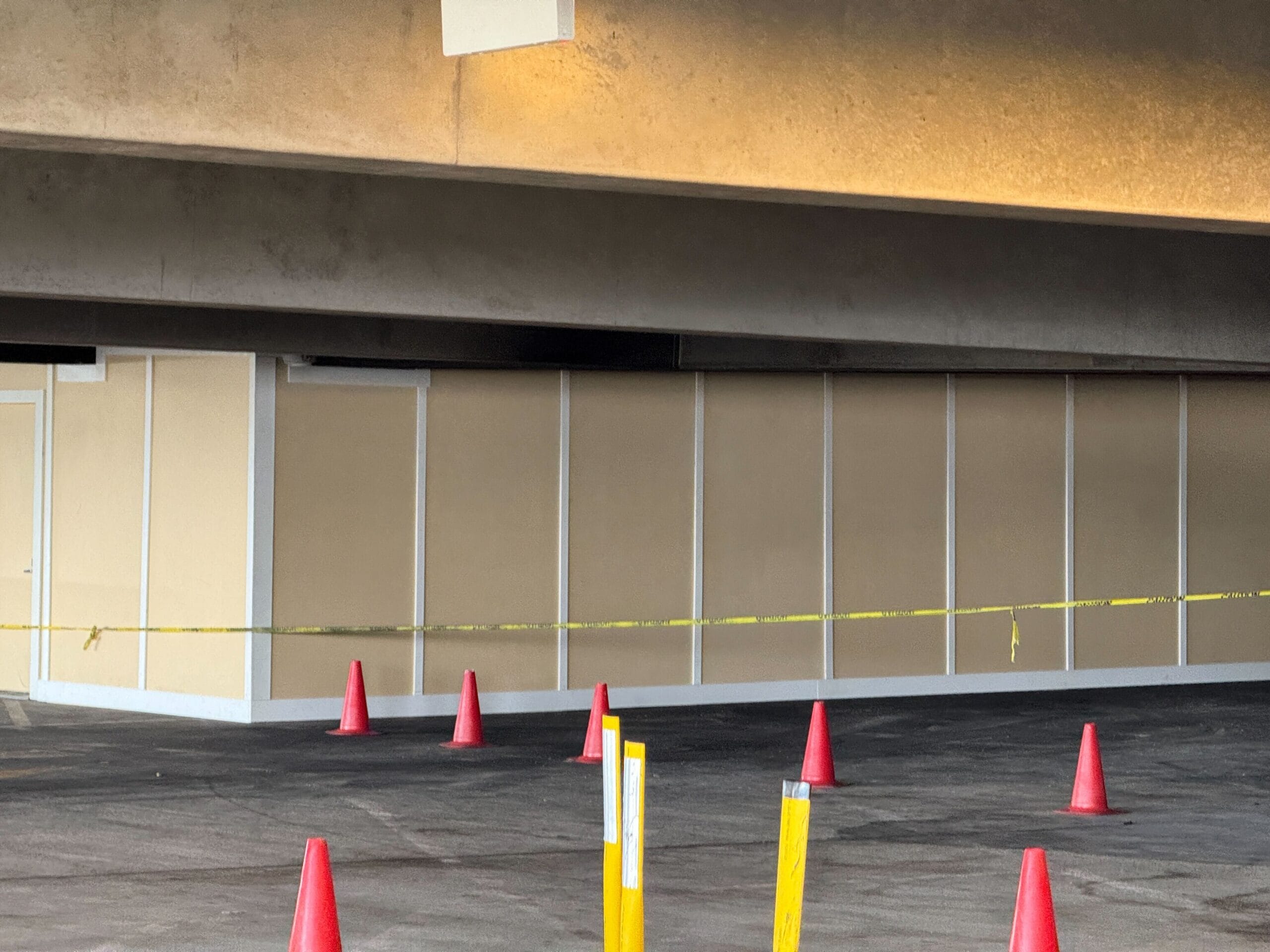 Parking area under construction with beige panels and surrounded by orange cones and yellow caution tape.