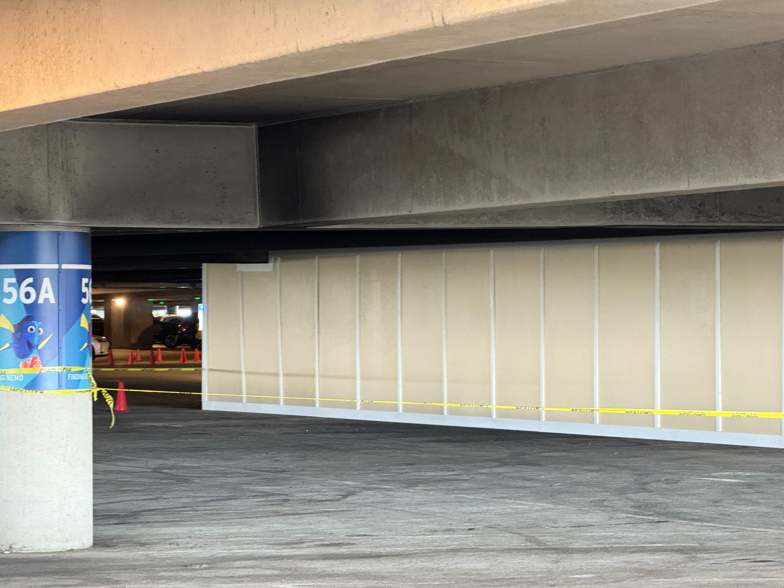 Concrete parking lot area with structural beams, sectioned off with caution tape and signs. Partial wall visible under the beams.