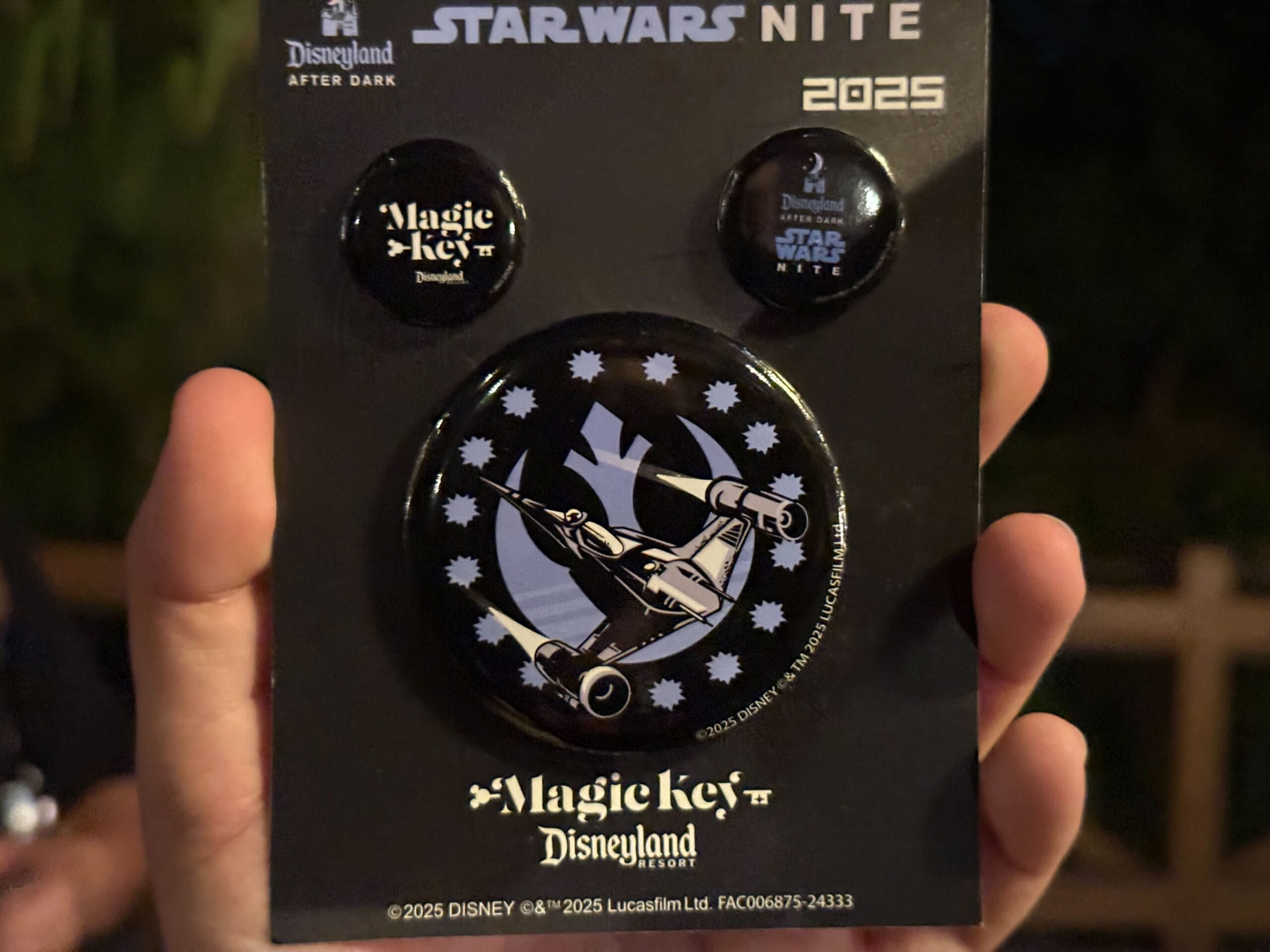 Person holding a card with three collectible buttons for "Star Wars Nite 2025" at Disneyland, including "Magic Key" and "Star Wars Nite" designs.