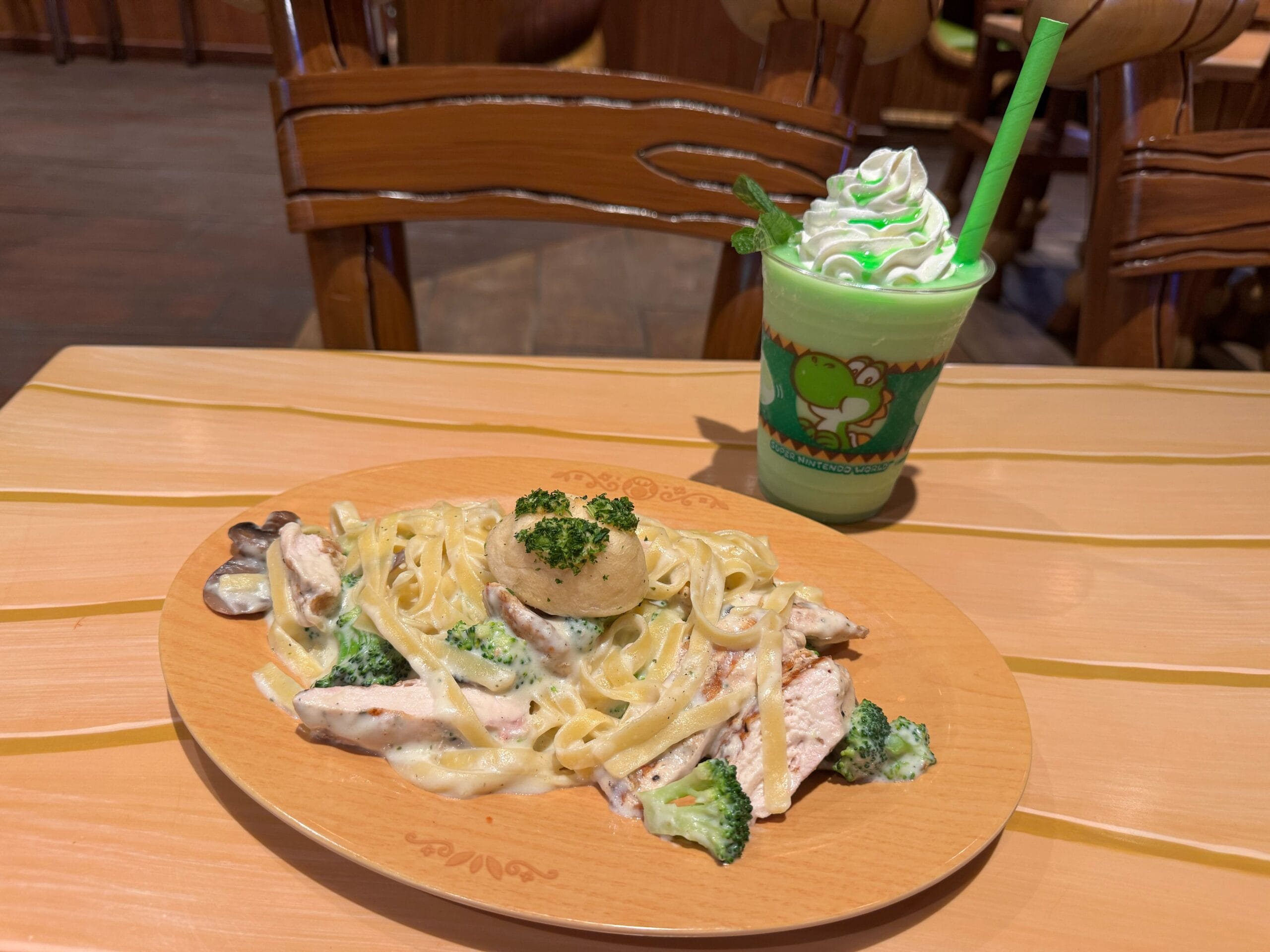 A plate of Yoshi-themed fettuccine pasta with chicken beside a green drink, perfect for Universal Fan Fest Nights.