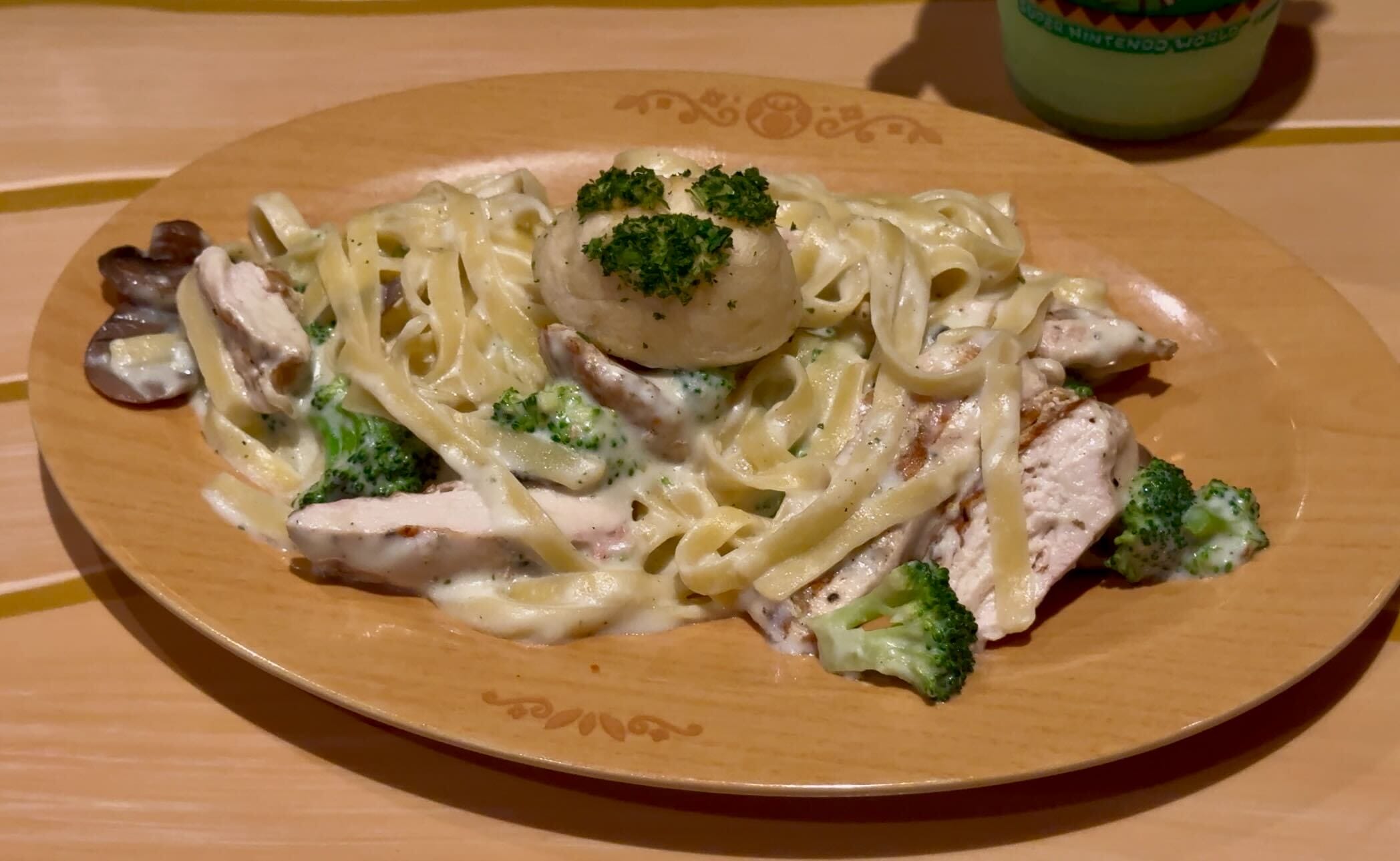 A plate of fettuccine Alfredo with grilled chicken, broccoli, and a mushroom, topped with a piece of broccoli.