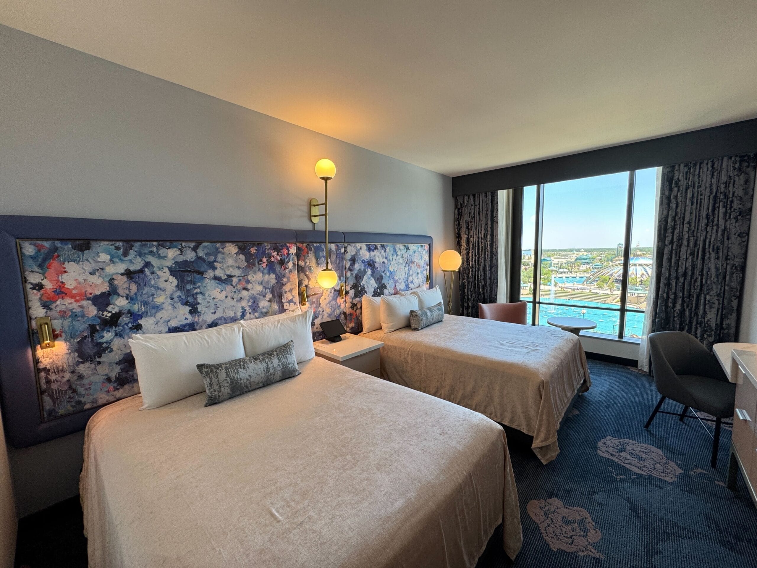 Park View Room at Universal Helios Grand Hotel features 2 Queen Beds, abstract headboard art, bedside lamps, a desk, and large windows offering stunning city and water views.
