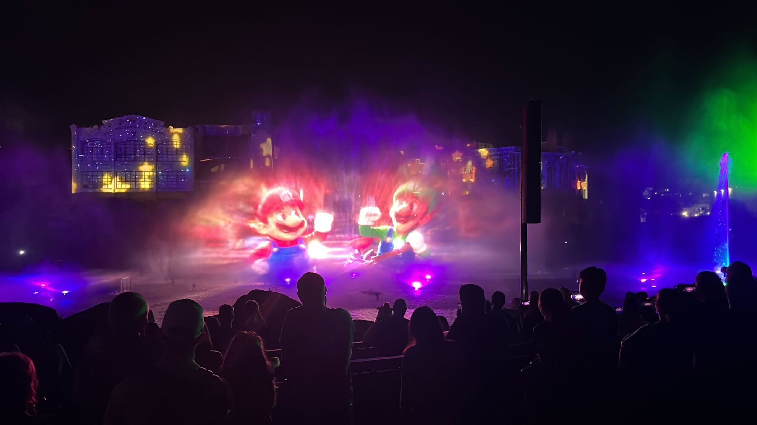 A silhouetted crowd marvels at the CineSational Symphonic Spectacular, a nighttime water and light show featuring projected cartoon characters, captivating visitors at Universal Studios Florida.