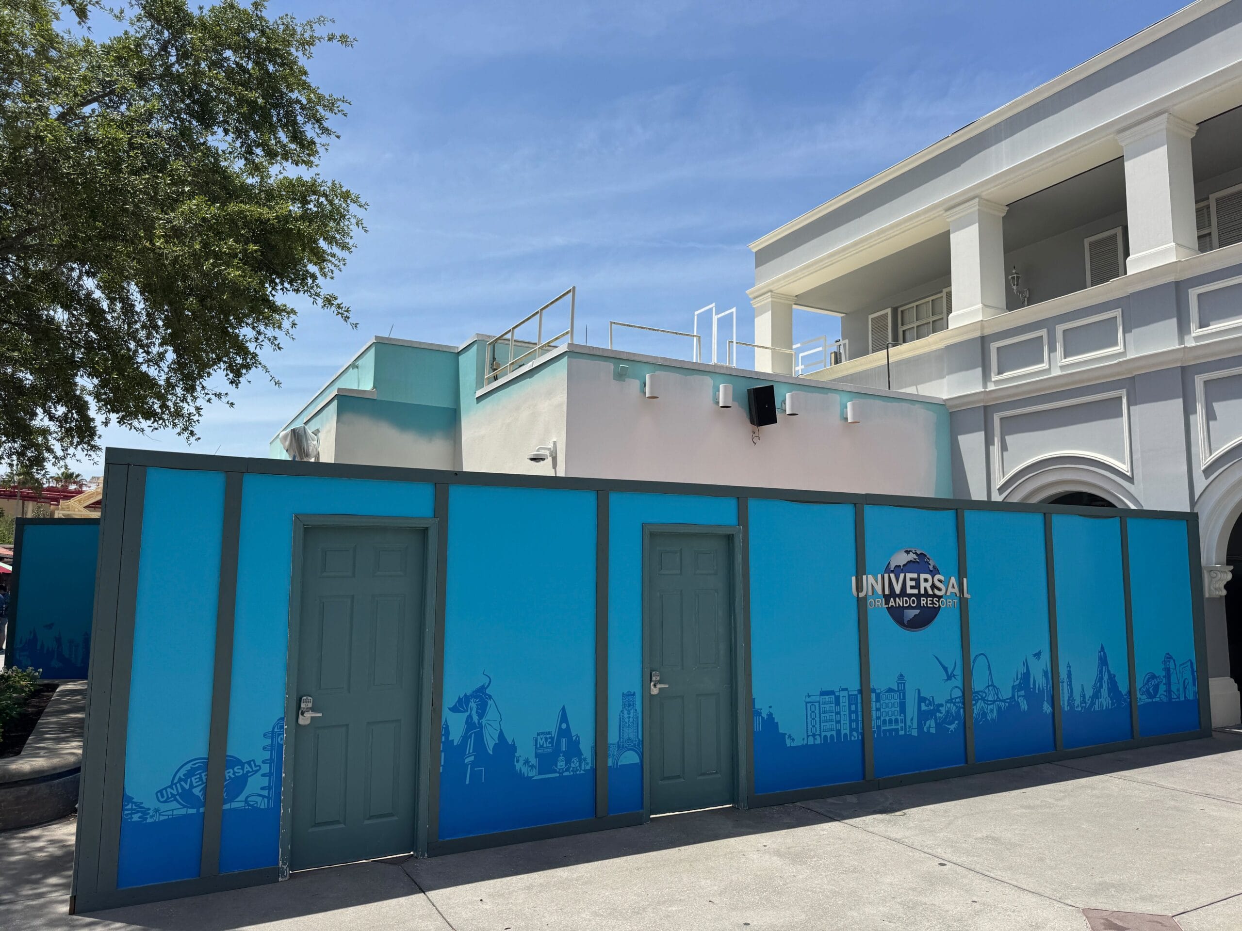 Blue construction walls with the Universal Orlando Resort logo mark an On Location shop construction on a sunny day.