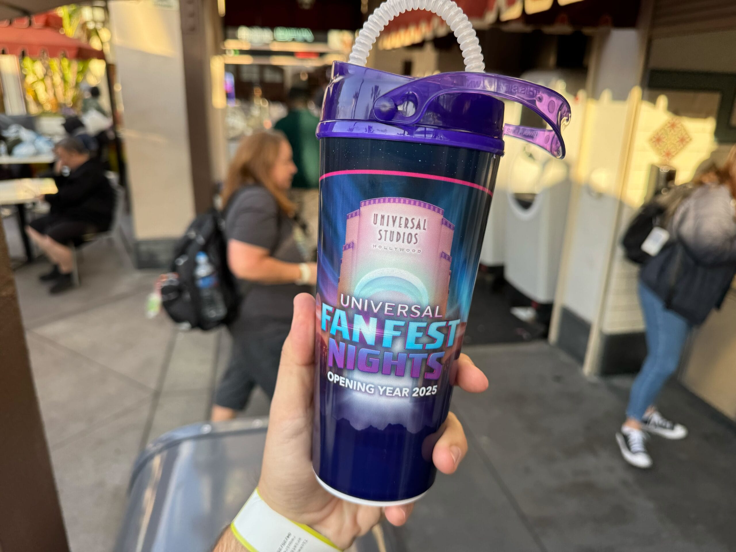 A hand holds a Universal Studios FanFest Nights cup with a straw. The cup says "Opening Year 2025.