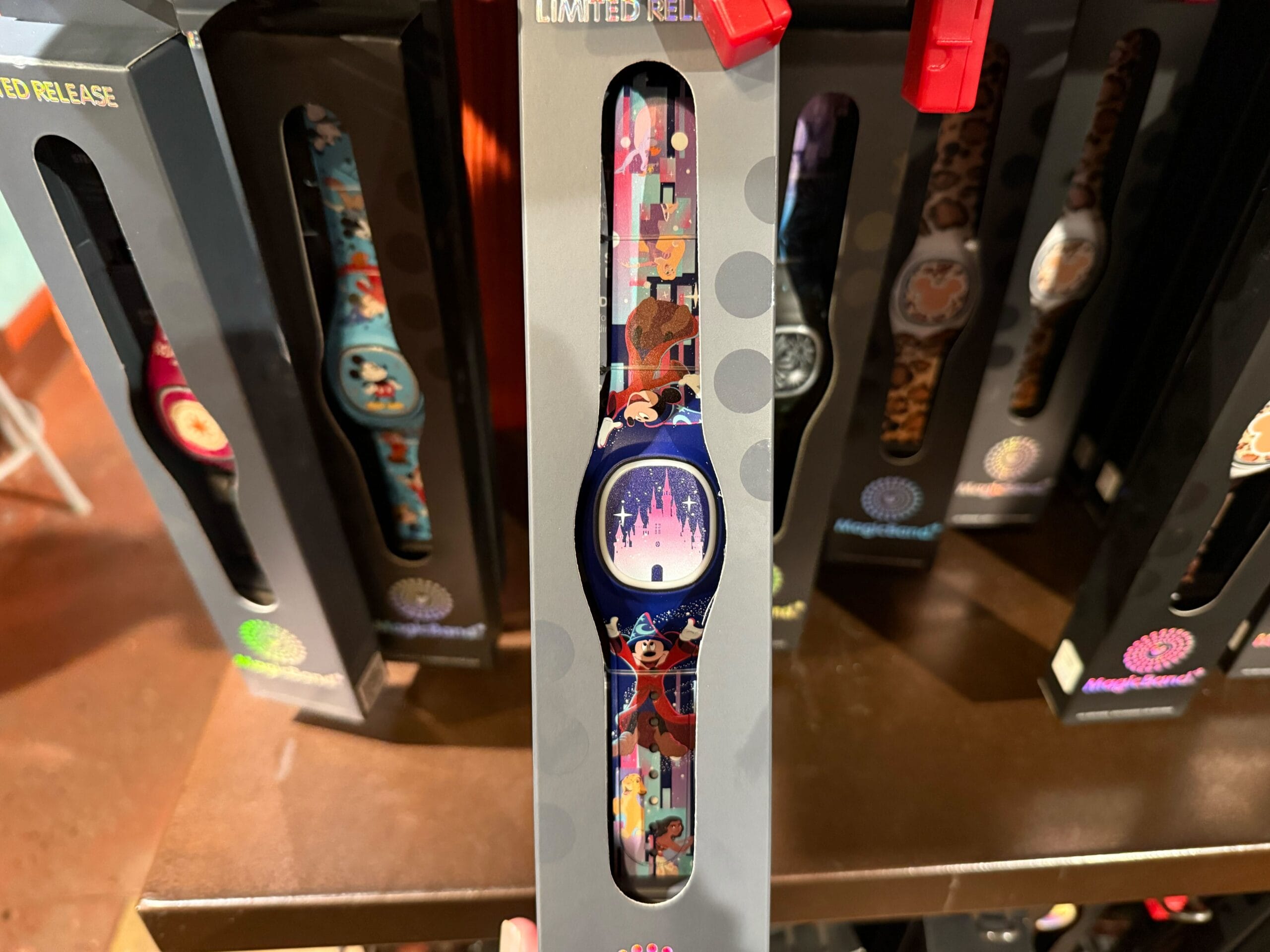 Enchantingly vibrant, this wristwatch comes in packaging adorned with a theme park design featuring a castle and character illustrations. Perfect for MagicBand+ enthusiasts, the watch is surrounded by others showcasing unique designs like Sorcerer Mickey and beloved Walt Disney World attractions.