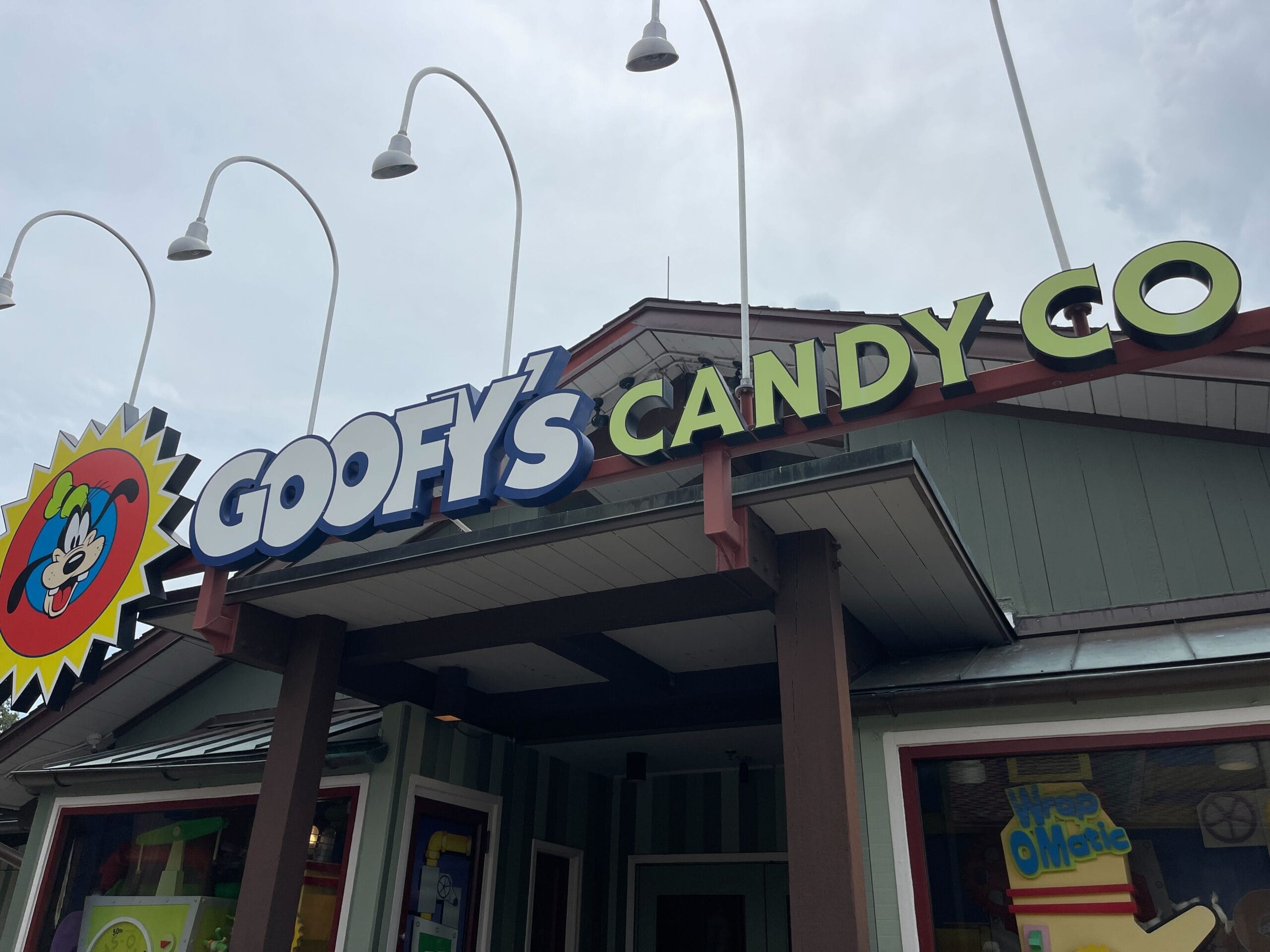 Under a cloudy sky at Disney Springs, discover the vibrant front view of Goofy's Candy Co. Adorned with colorful signage featuring the whimsical Goofy, it's the perfect spot to celebrate National Caramel Day.