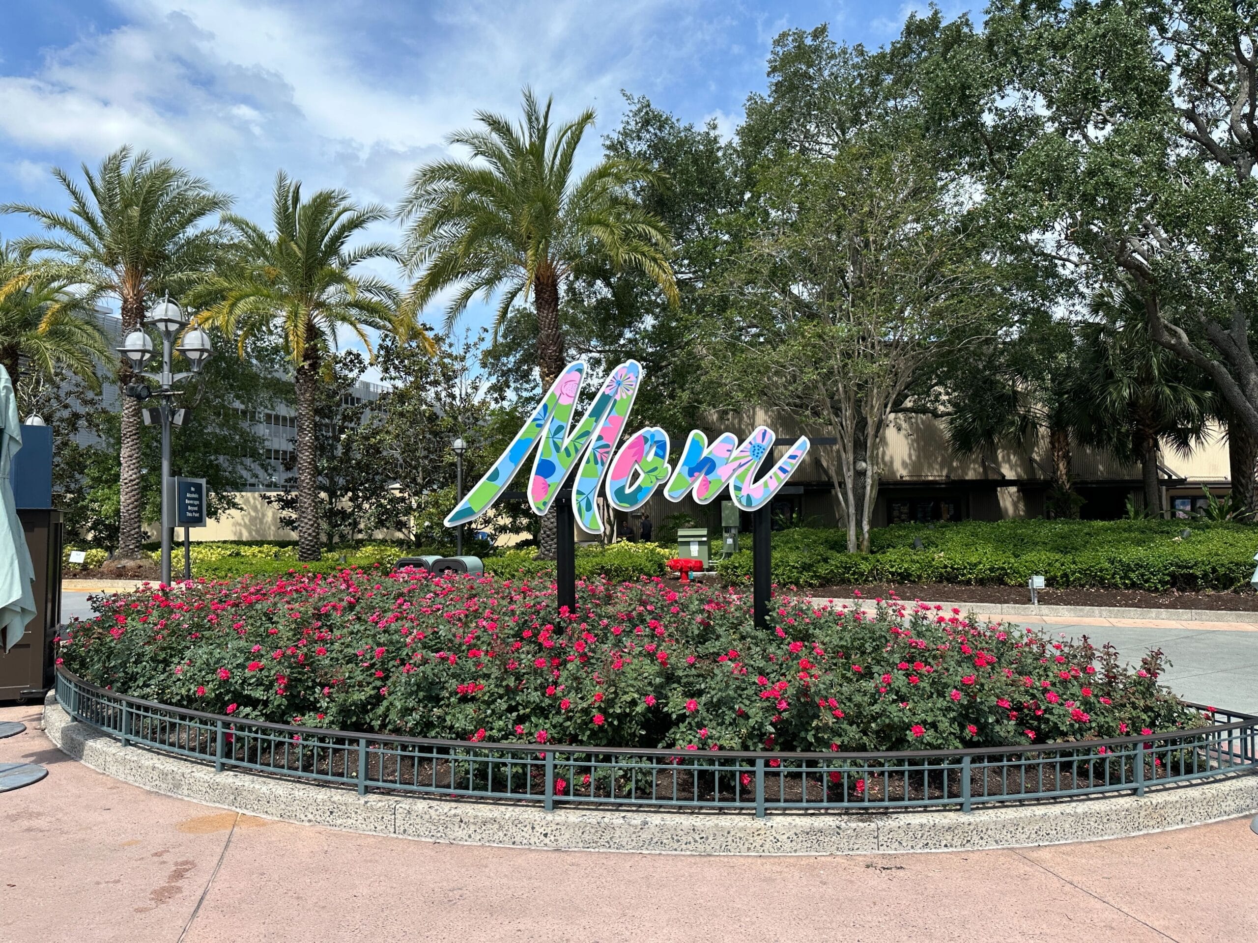 A colorful "Mom" sign in a flower bed makes the perfect Mother's Day photo op at Disney Springs under a partly cloudy sky.
