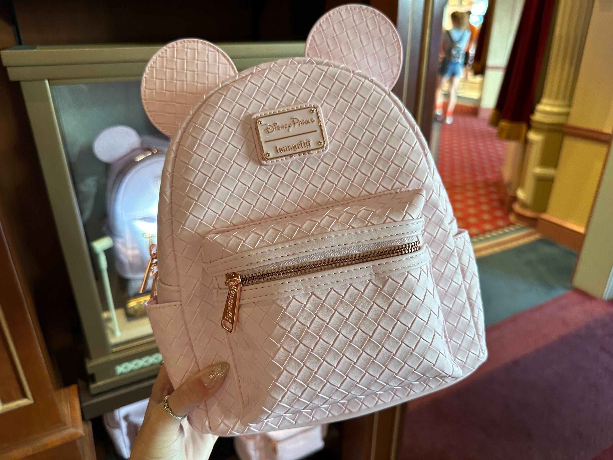 Displayed in a store is a Pink Loungefly mini backpack with mouse ears, featuring a woven pattern and a front zipper pocket.