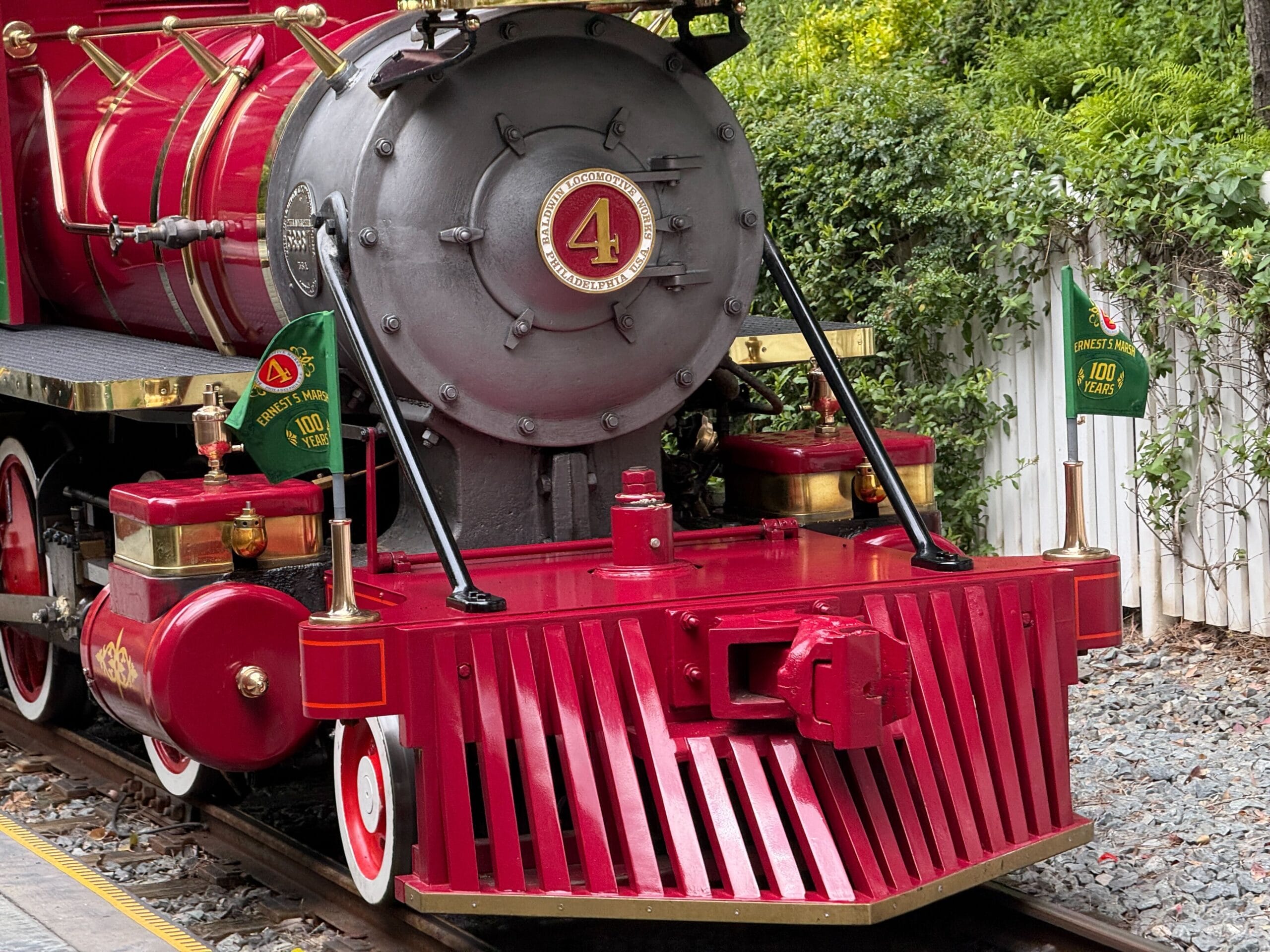 Red steam locomotive with a large number 4 on the front, green flags, and white-rimmed wheels on railroad tracks.