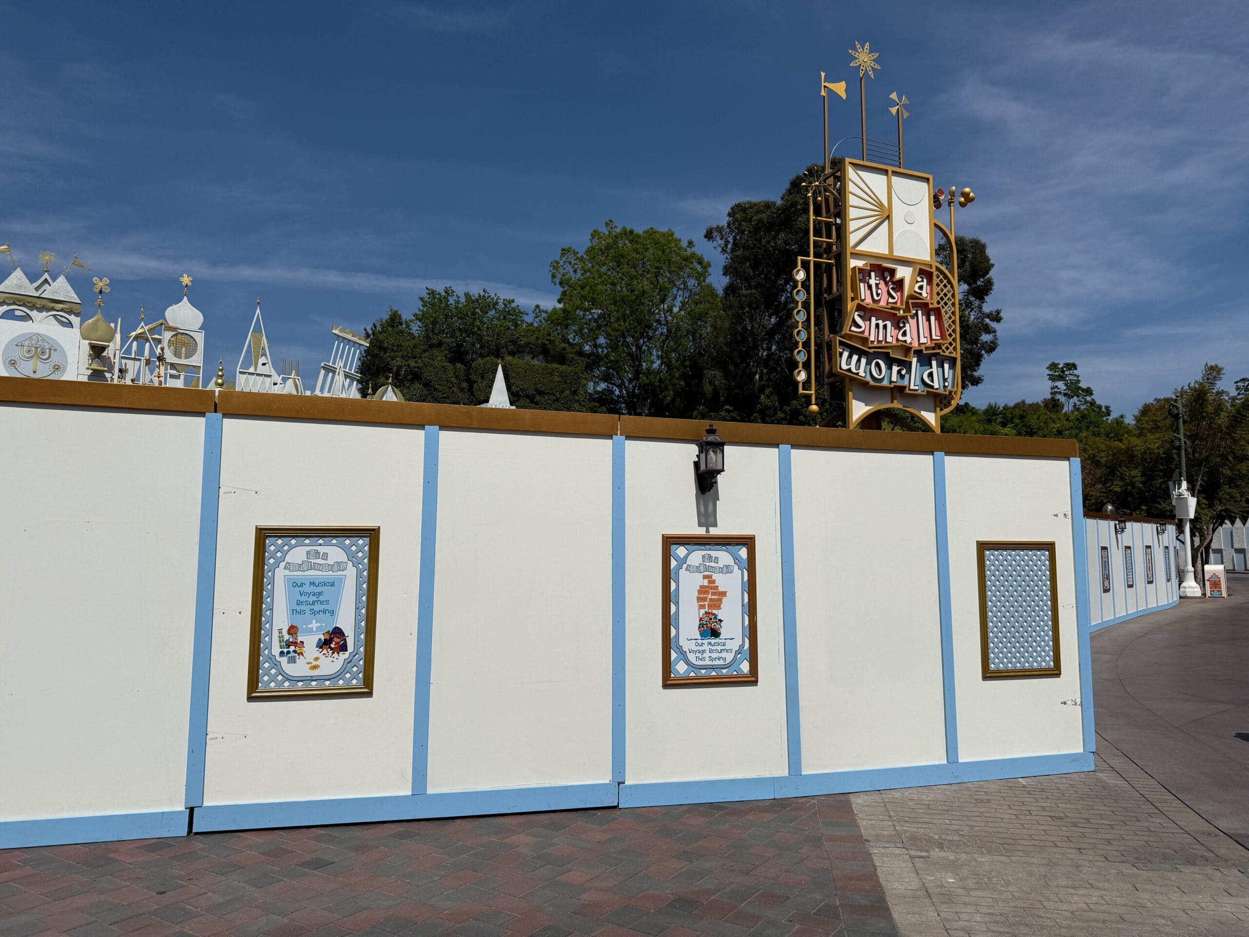 The entrance to Disneyland Park's "It's a Small World" is currently obscured by construction walls, adorned with themed posters, while the iconic ride's sign peeks out from the background.