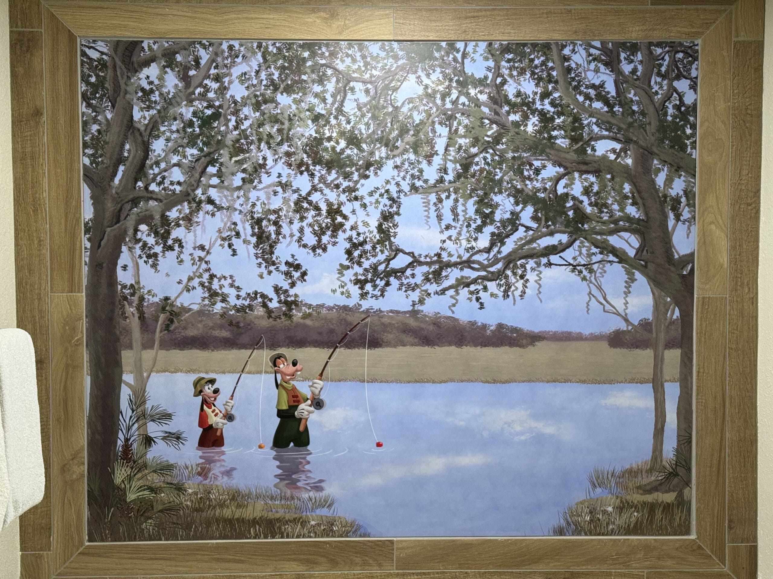 Artwork of two cartoon characters fishing in a lake, encapsulating the serene charm of Disney's Hilton Head Island Resort. Surrounded by trees with draping branches and a calm landscape in the background, it's reminiscent of peaceful moments from a tour at the remodeled 1-bedroom villa.