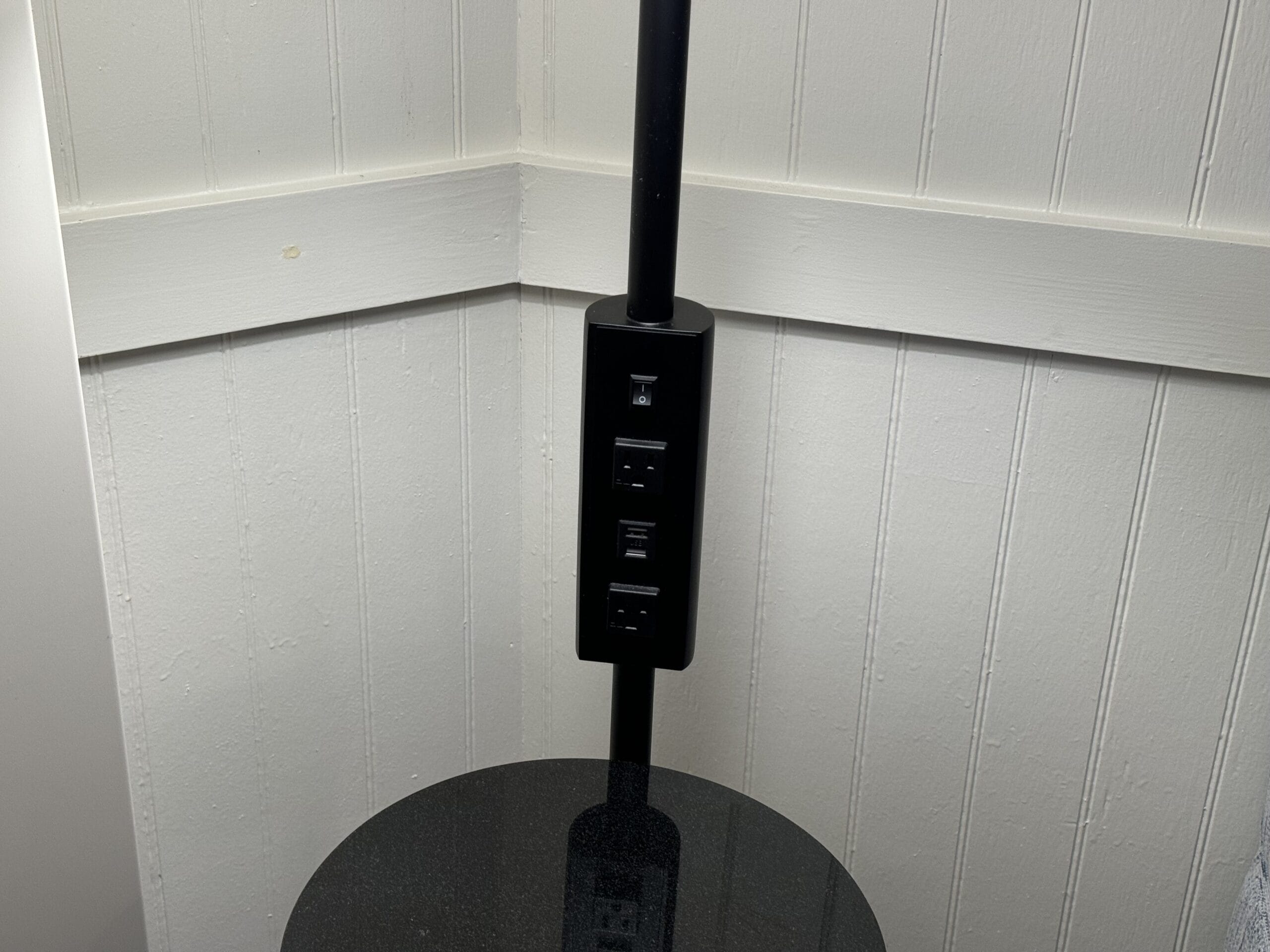 Black floor lamp with built-in electrical and USB outlets stands elegantly against a white paneled wall, much like the stylish touches you might find in a remodeled 1-bedroom villa at Disney's Hilton Head Island Resort.