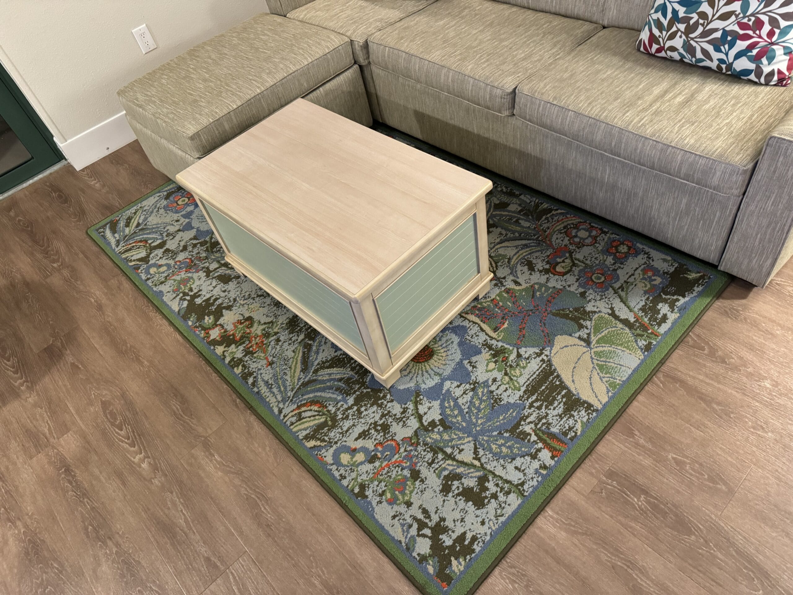 A newly remodeled 1-bedroom villa features a charming wooden coffee table on a patterned rug beside a gray sectional sofa with a floral cushion, all set on a polished wooden floor. It's like stepping into Disney's Hilton Head Island Resort for an enchanting tour of comfort and style.