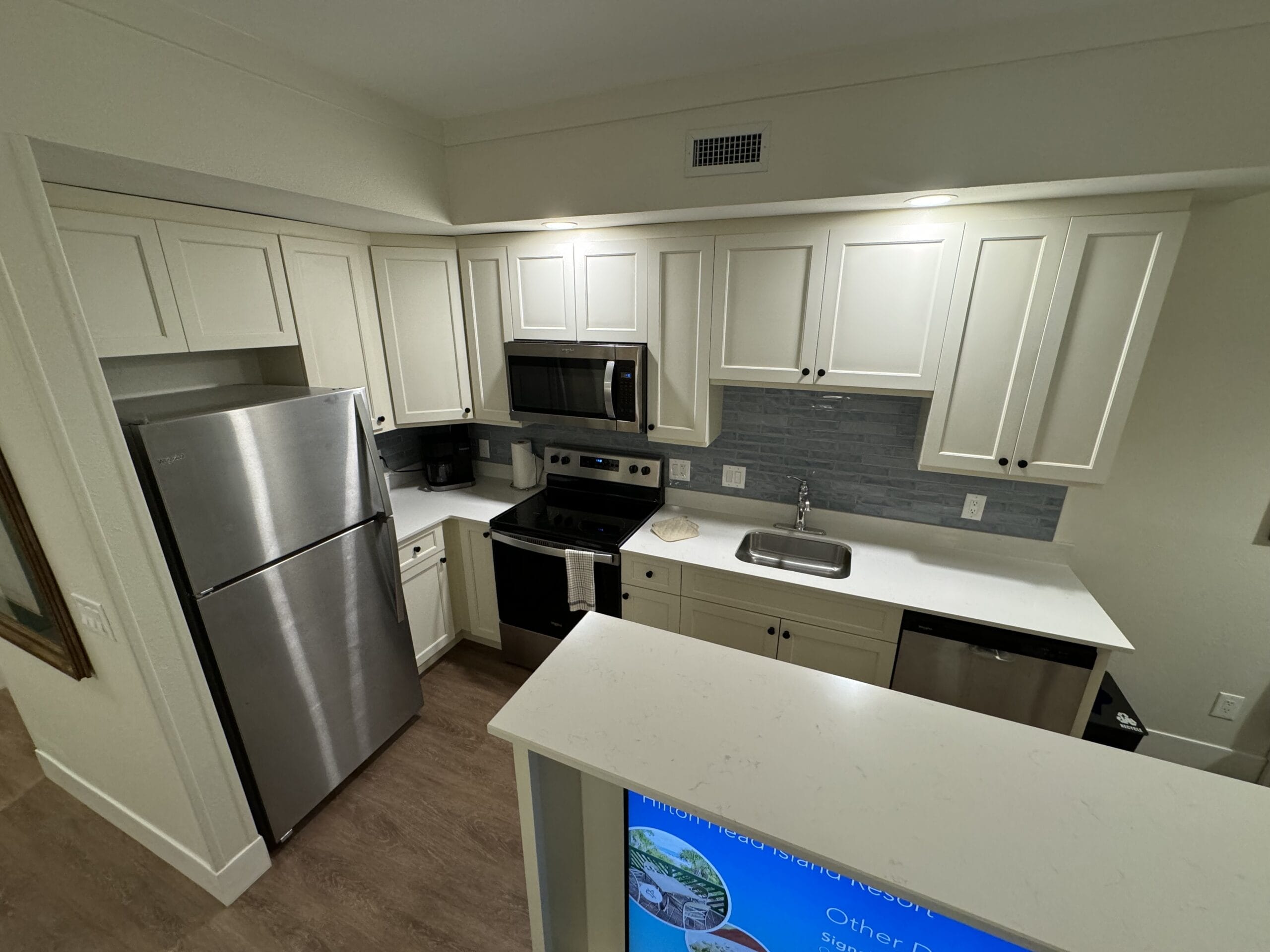 This remodeled 1-bedroom villa features a modern kitchen with white cabinets and stainless steel appliances, including a fridge and oven. Enjoy the wood-paneled floor and blue backsplash as you prepare meals just like in Disney's Hilton Head Island Resort.