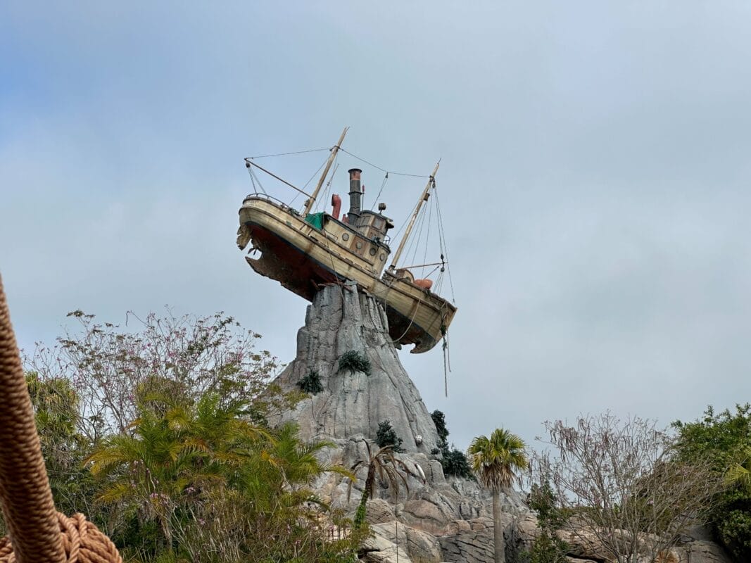 A boat sits atop a rocky cliff with trees and greenery, under clouds—like a scene from a Disney lawsuit story.