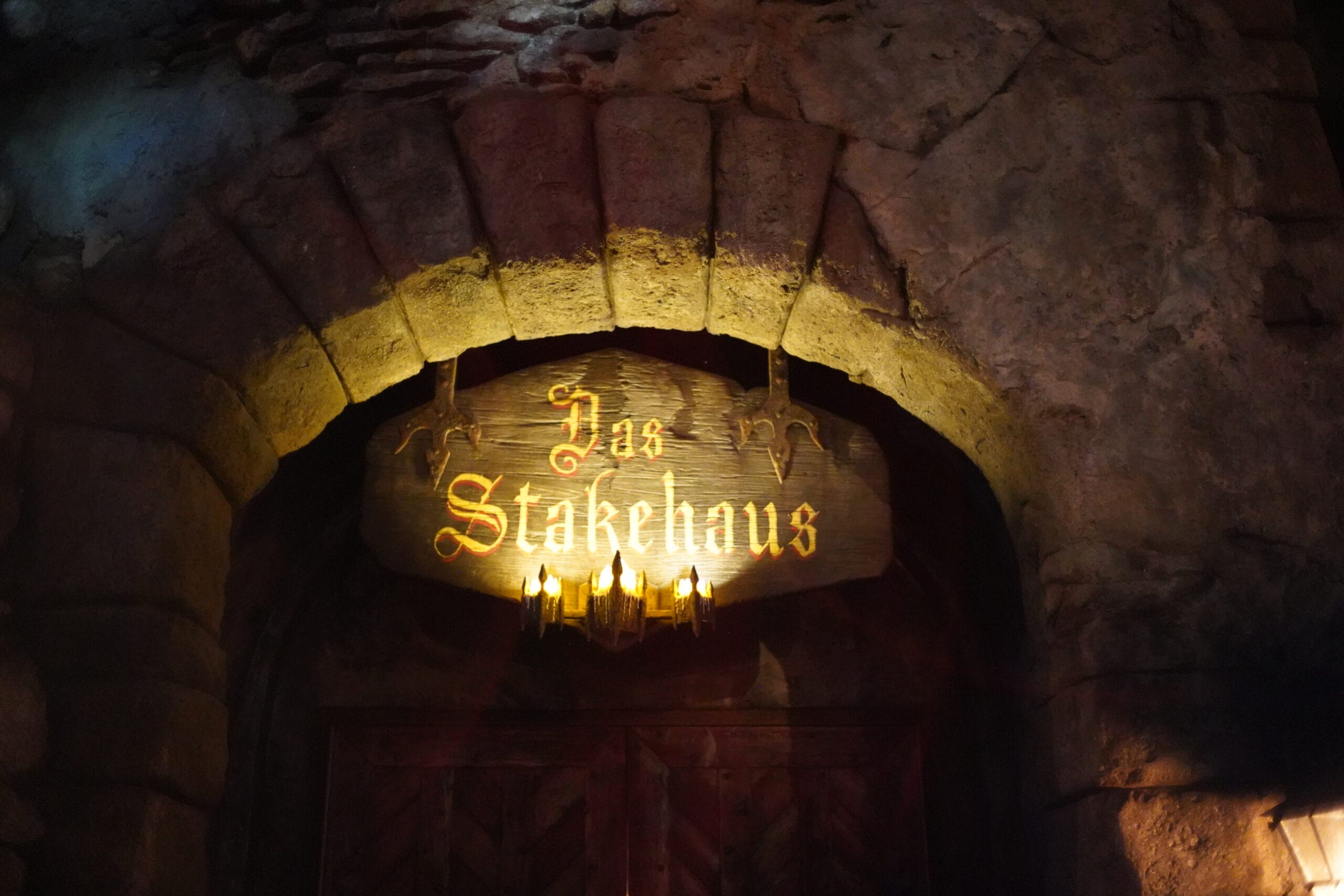 A wooden “Das Stakehaus” sign glows above a stone archway, illuminated by three lights underneath.