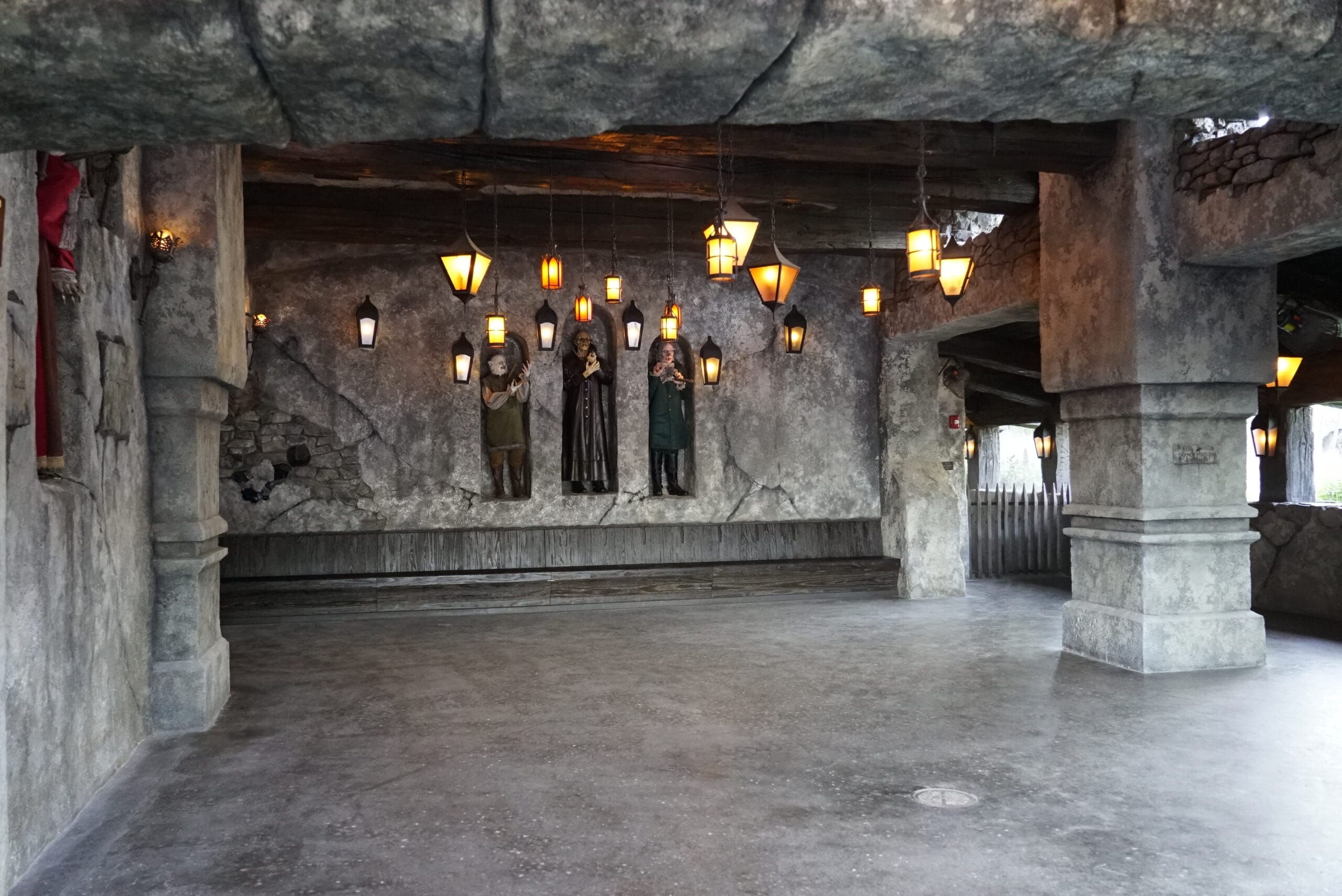 A stone room with hanging lanterns and three statues, evoking a medieval vibe fit for Das Stakehaus.