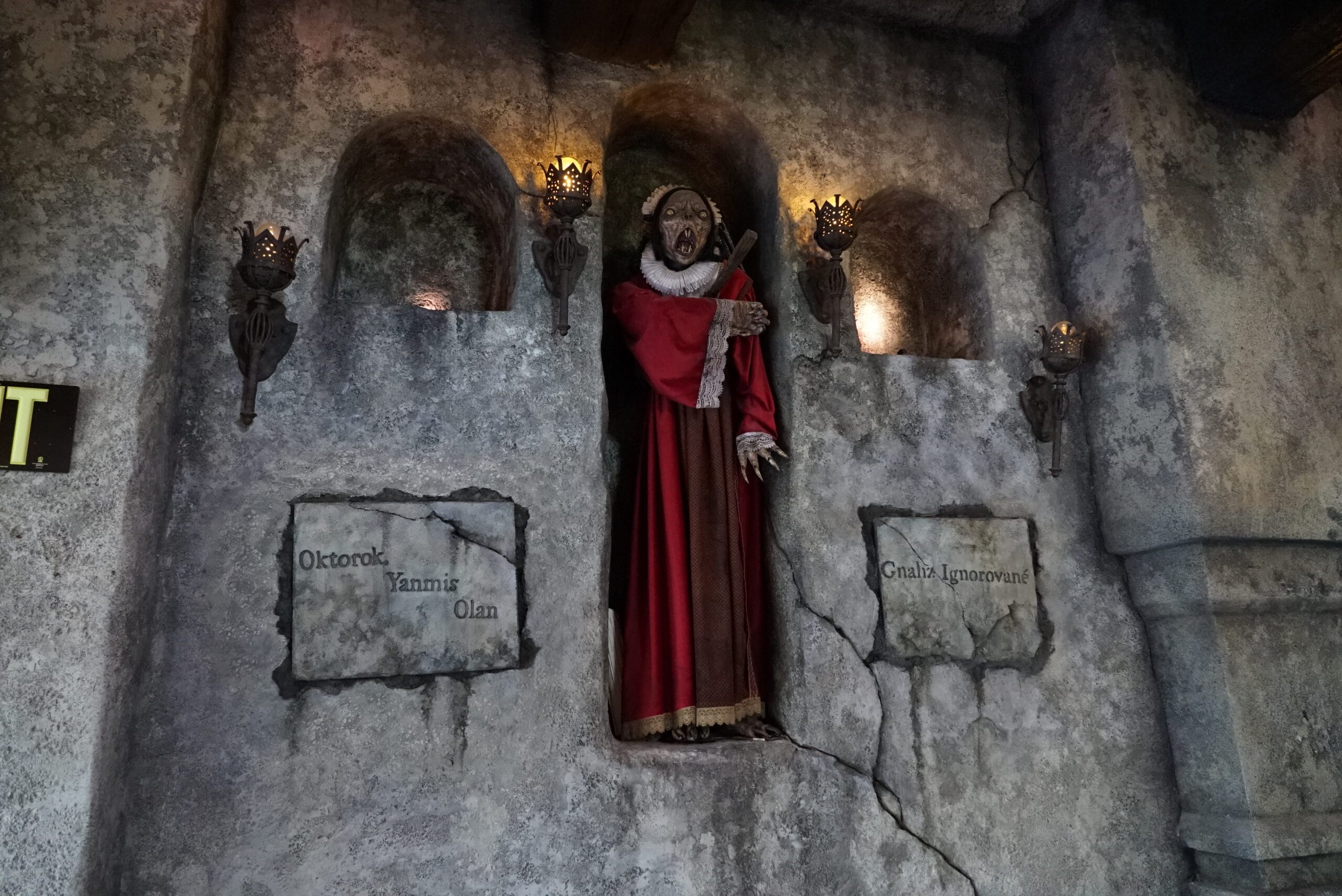 A statue in red robes stands in a stone alcove at Das Stakehaus, surrounded by torches and inscribed plaques.