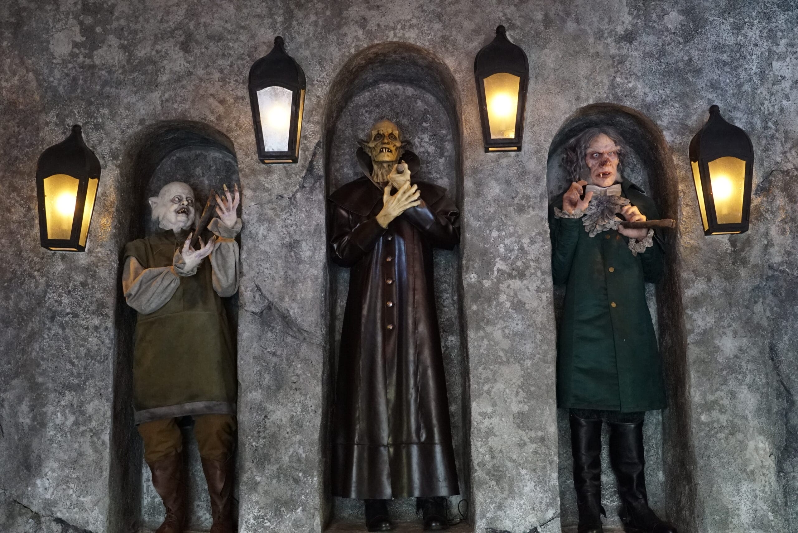 Three eerie, goblin-like statues stand in stone alcoves at Das Stakehaus under glowing lanterns.