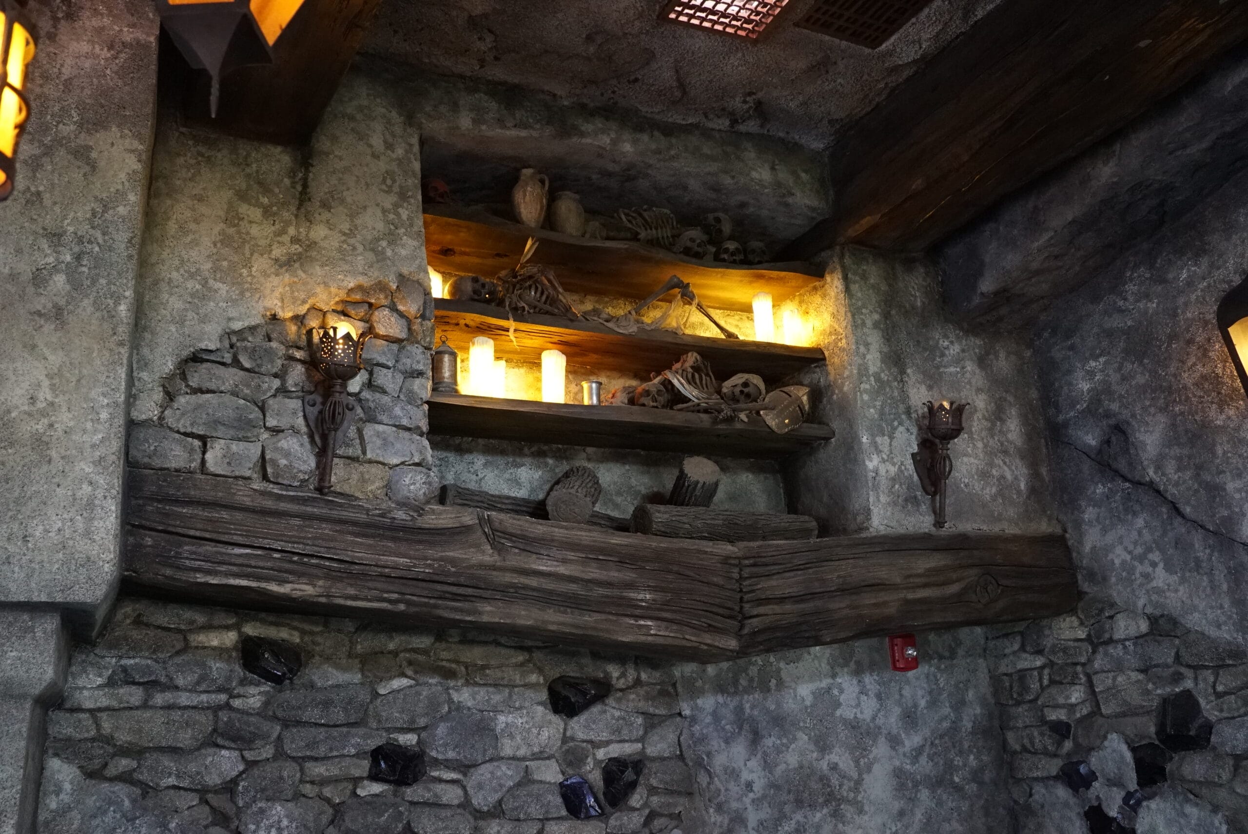 Stone wall with wooden shelves, candles, and skeletons in Das Stakehaus’s dimly lit, medieval-style room.