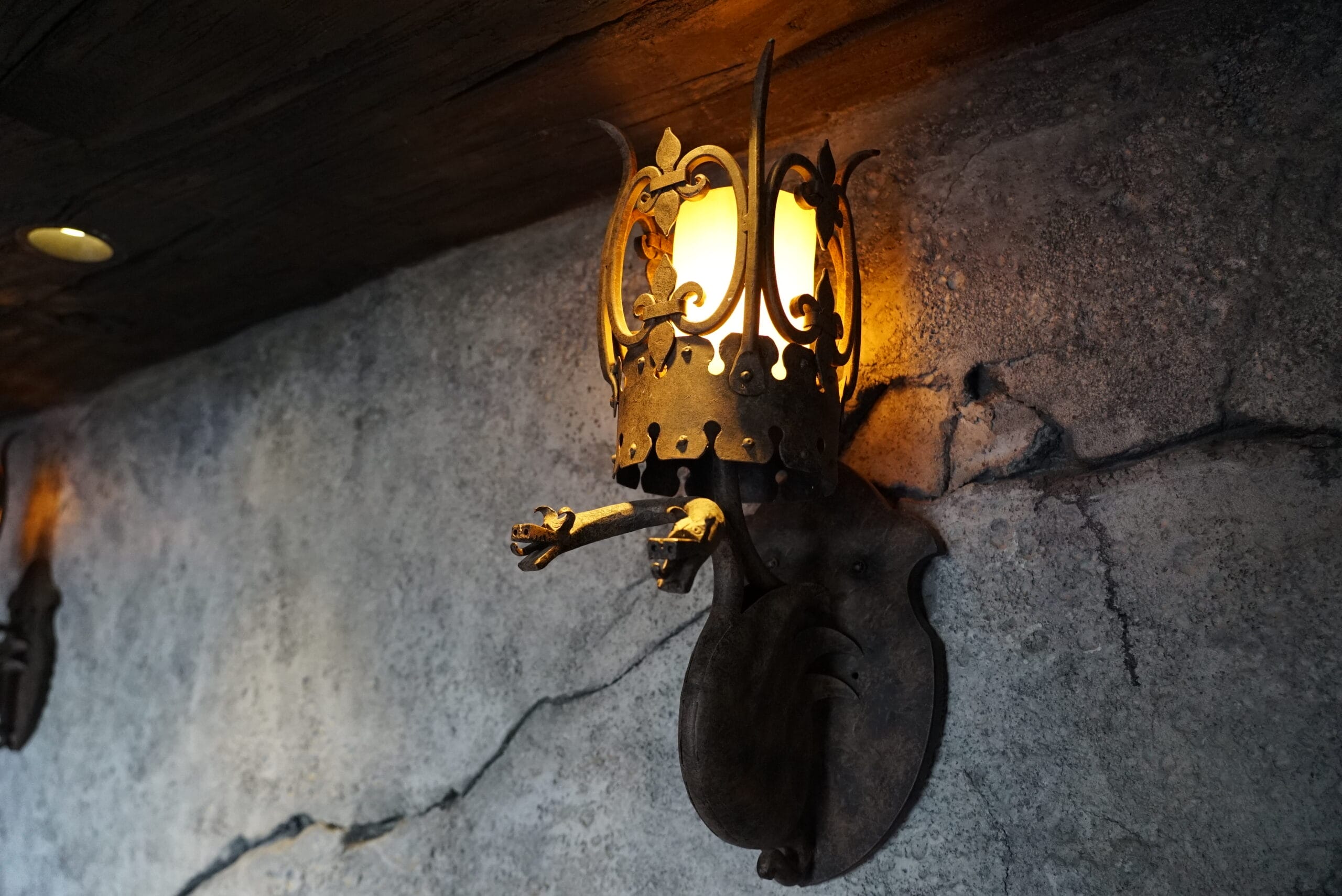 Rustic, medieval-style wall sconce with a glowing light, perfect for Das Stakehaus, mounted on a cracked stone wall.