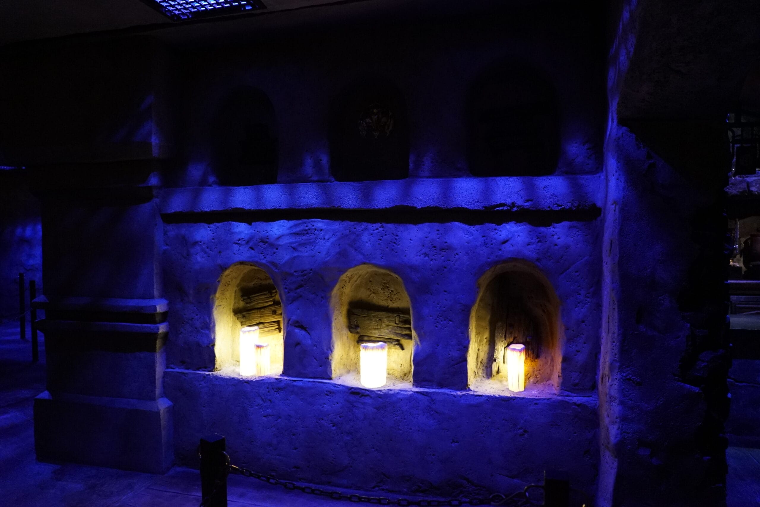 Three illuminated niches in a stone wall glow under blue and yellow lighting at Das Stakehaus in a darkened room.