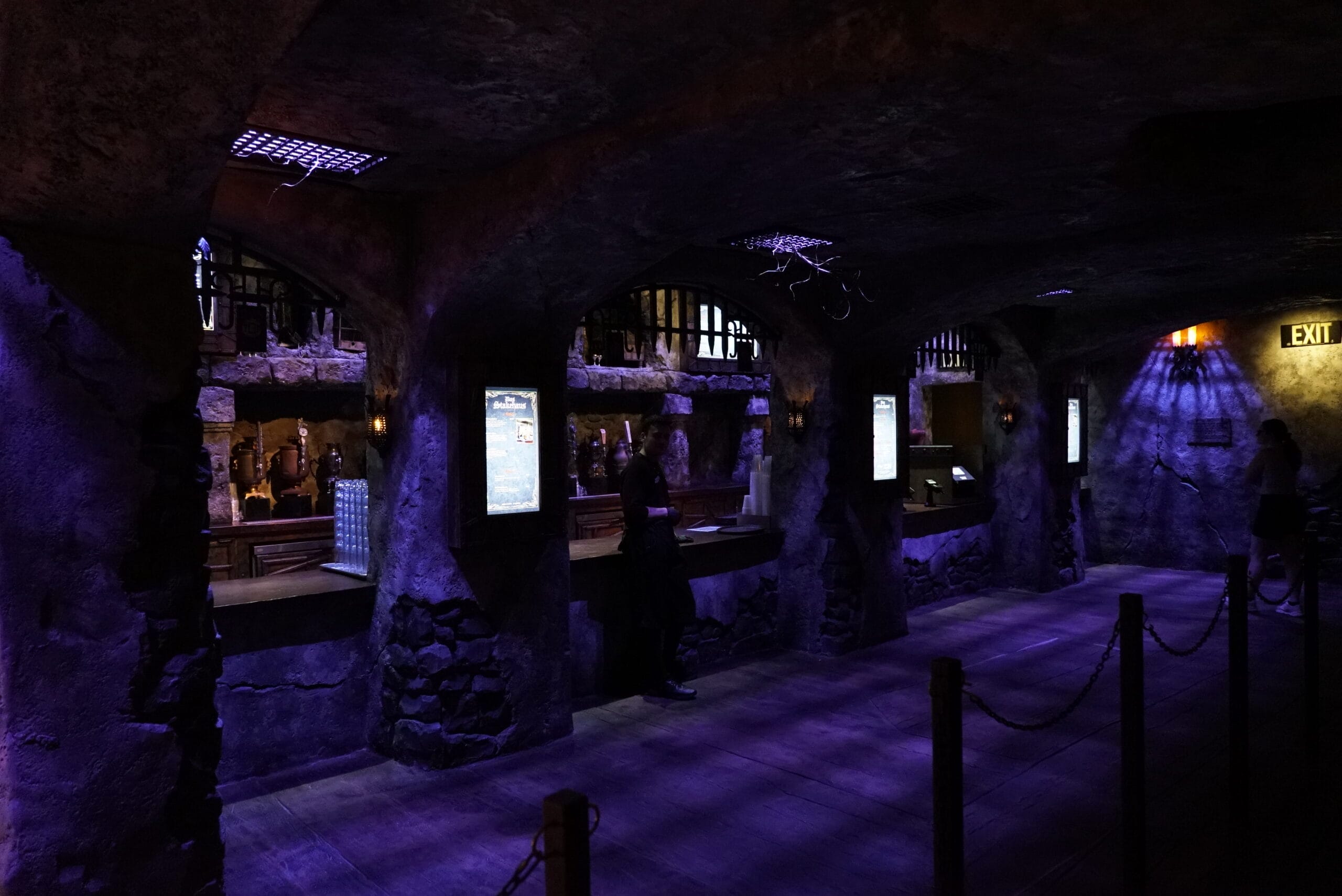 Dimly lit, medieval-style tavern with stone arches, digital menus, and a lone figure at Das Stakehaus’s counter.