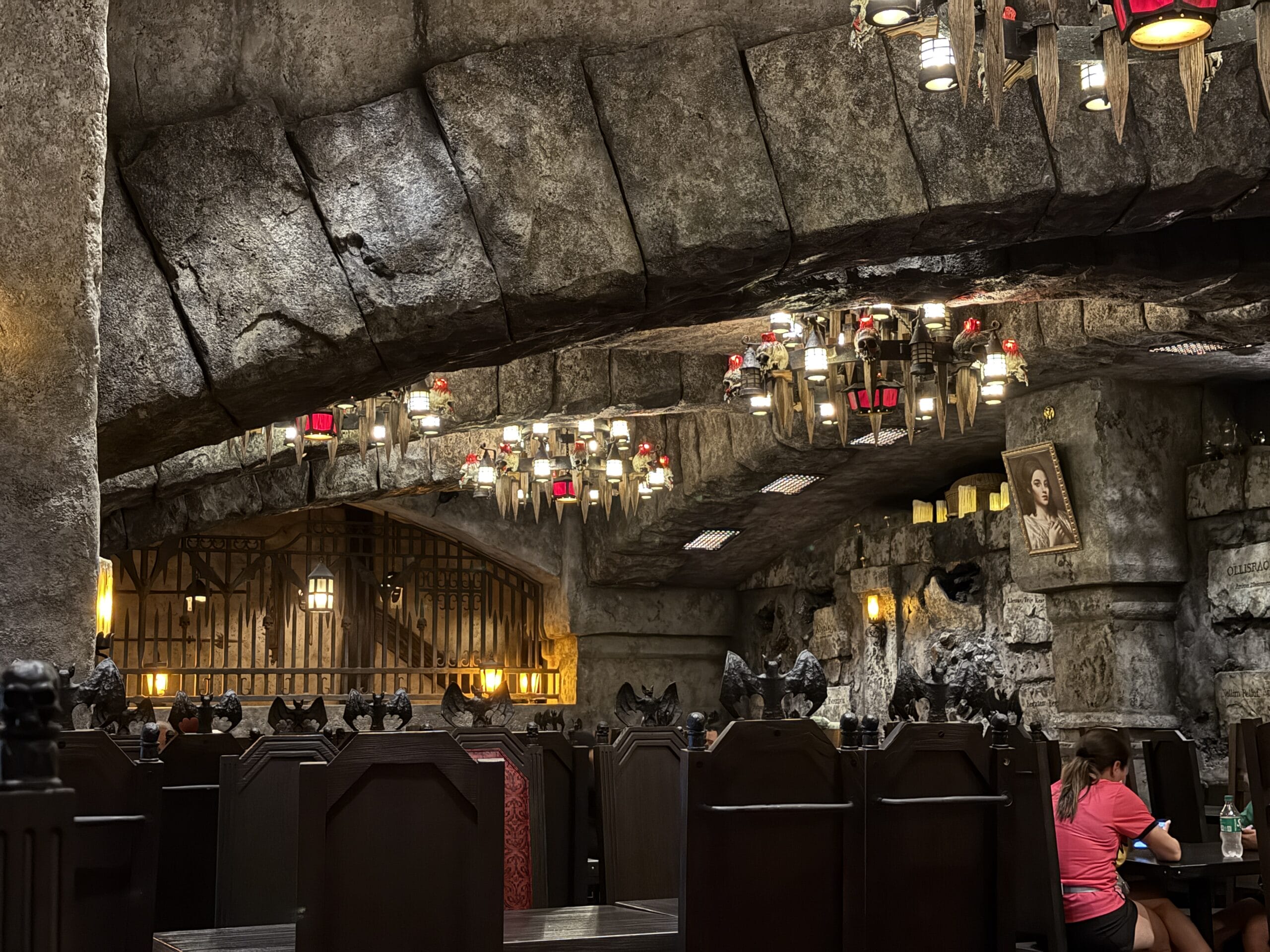 A stone-walled, dimly lit restaurant, Das Stakehaus features gothic chandeliers and a portrait above dark tables.