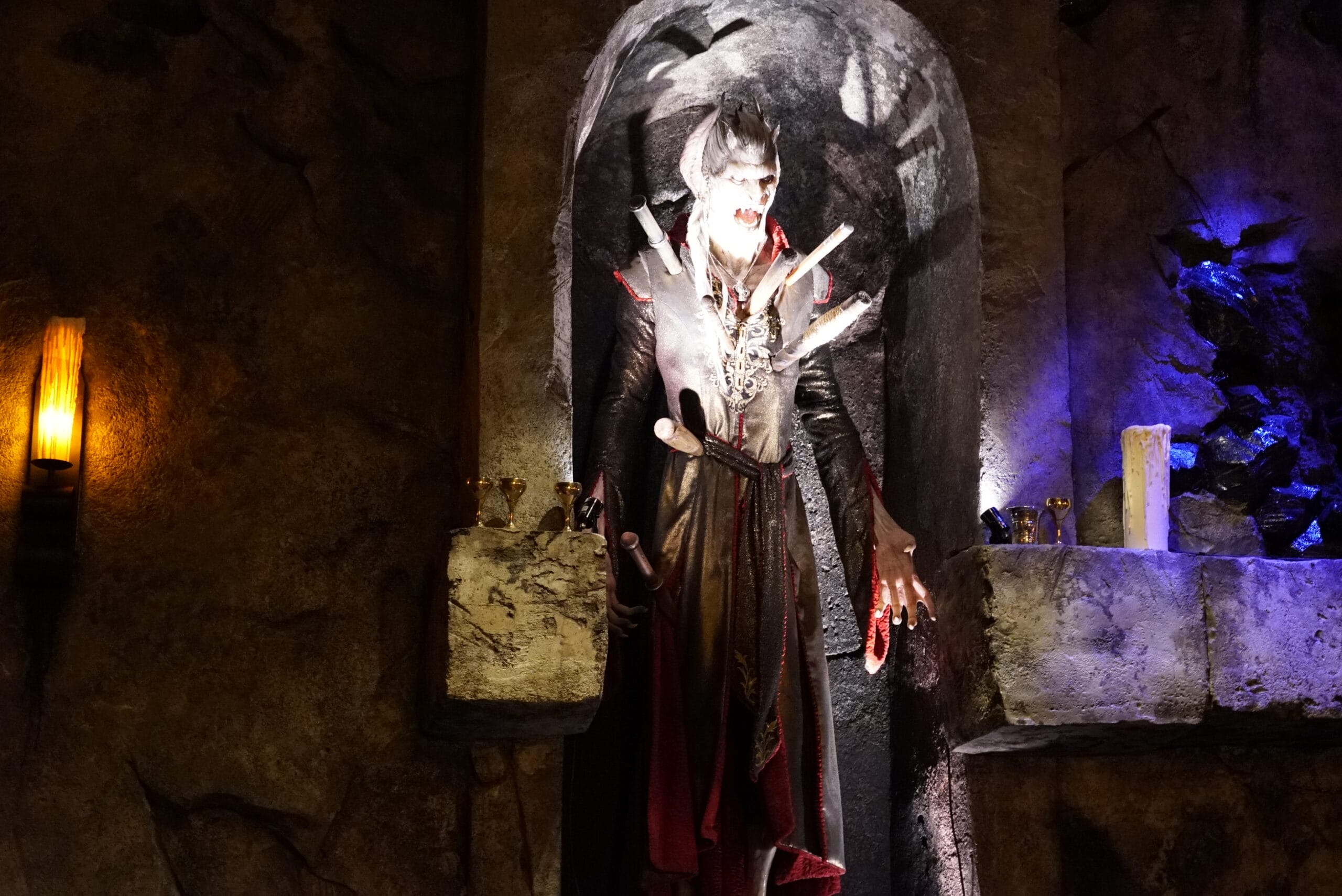 A vampire statue with fangs stands in Das Stakehaus alcove, lit by candles and dramatic lighting.