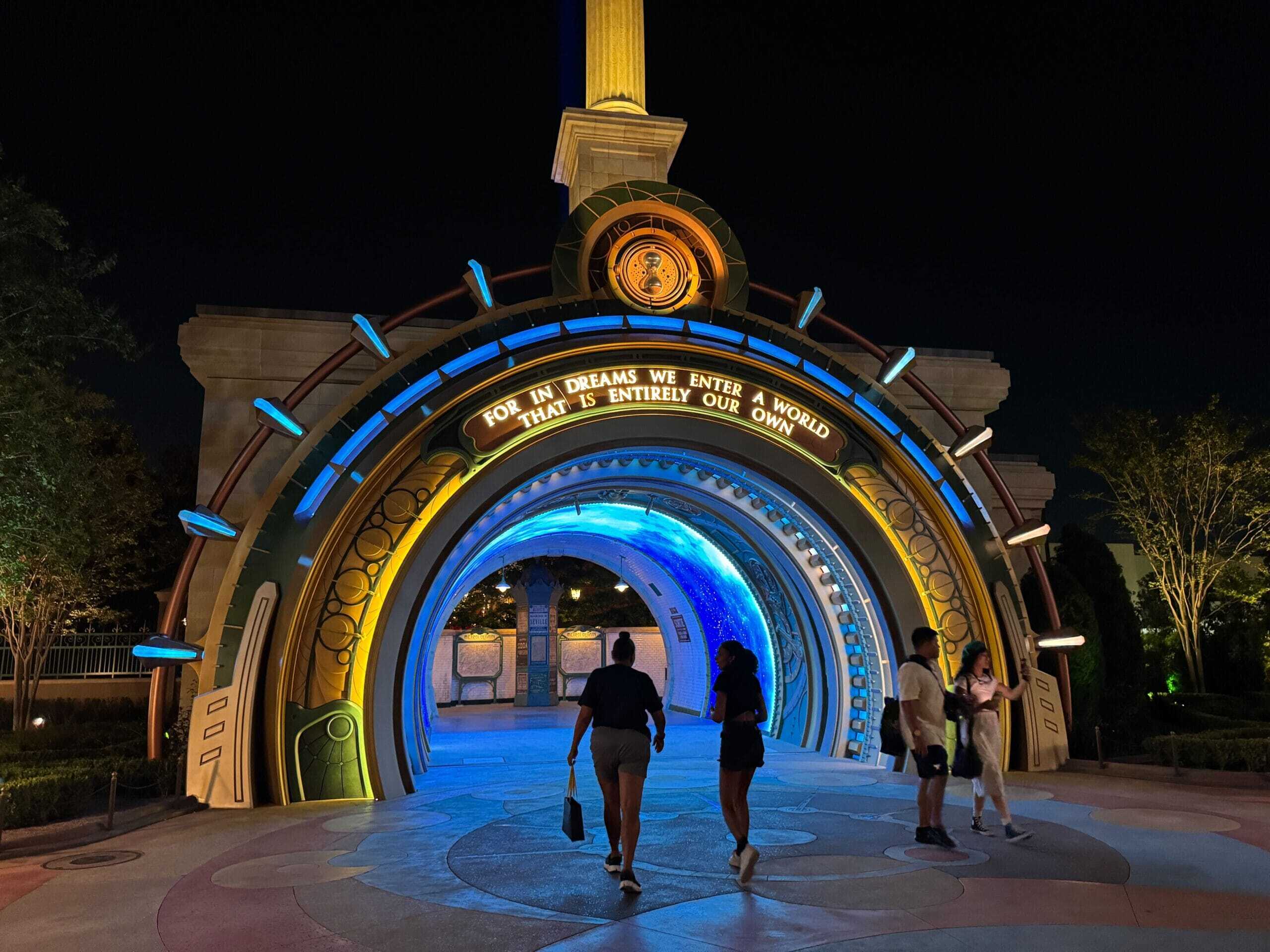 People walk through a brightly lit, futuristic archway at night during Epic Universe annual passholder previews.
