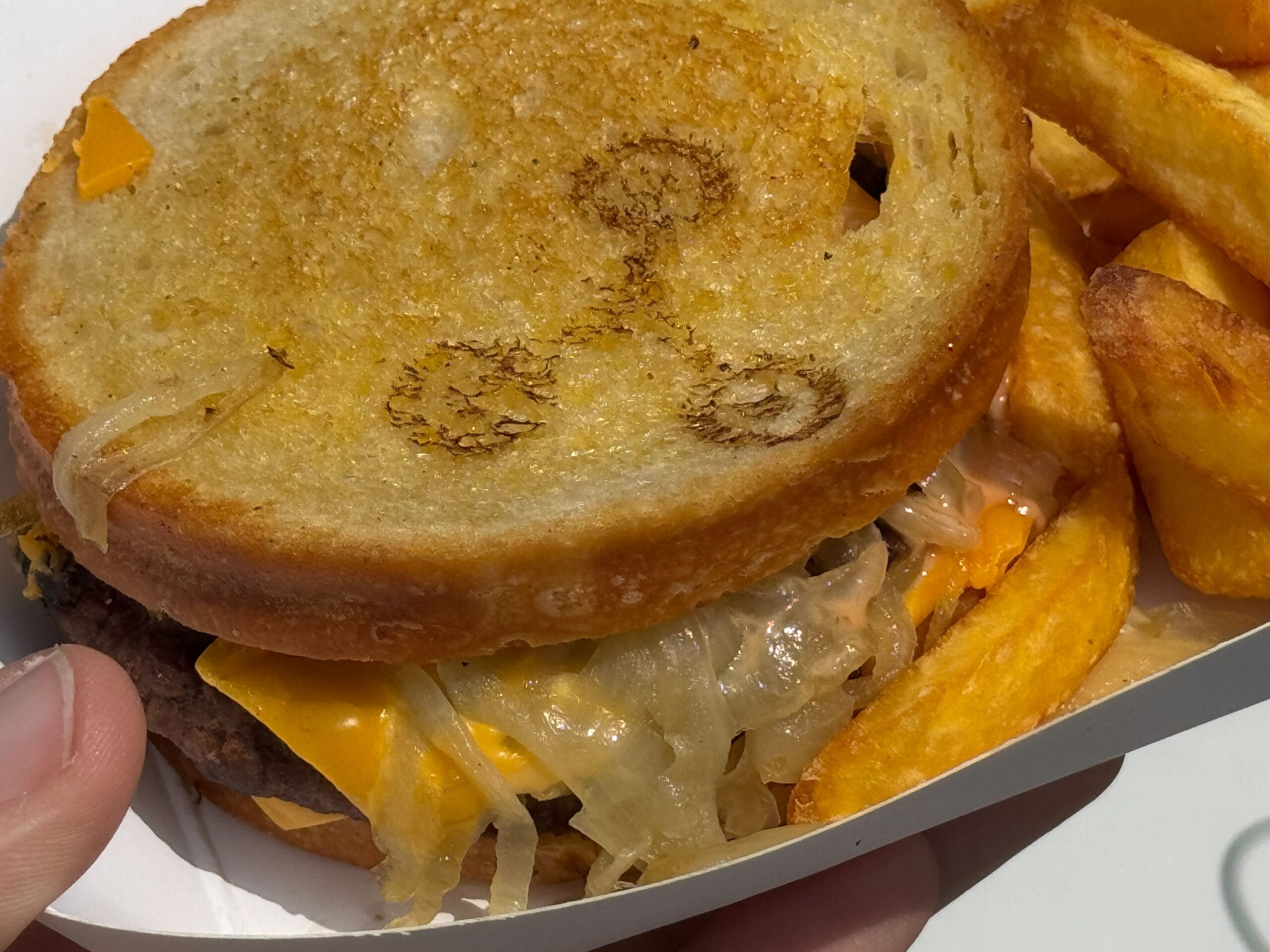 A grilled cheese burger with melted cheese, onions, and thick fries in a white tray.