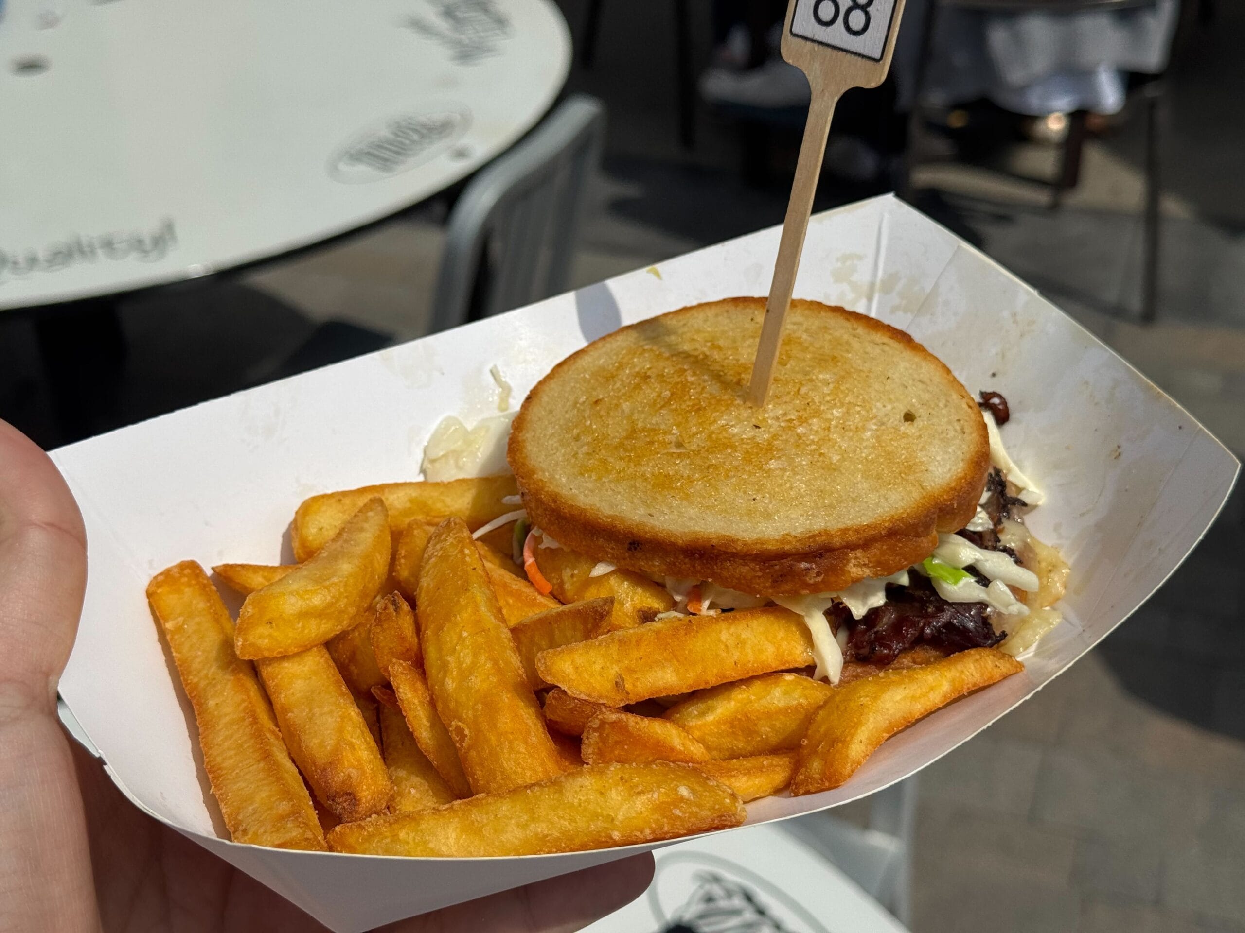 A hand holds a tray with crispy fries and a sandwich, serving up classic comfort with a tasty BTTF food twist.