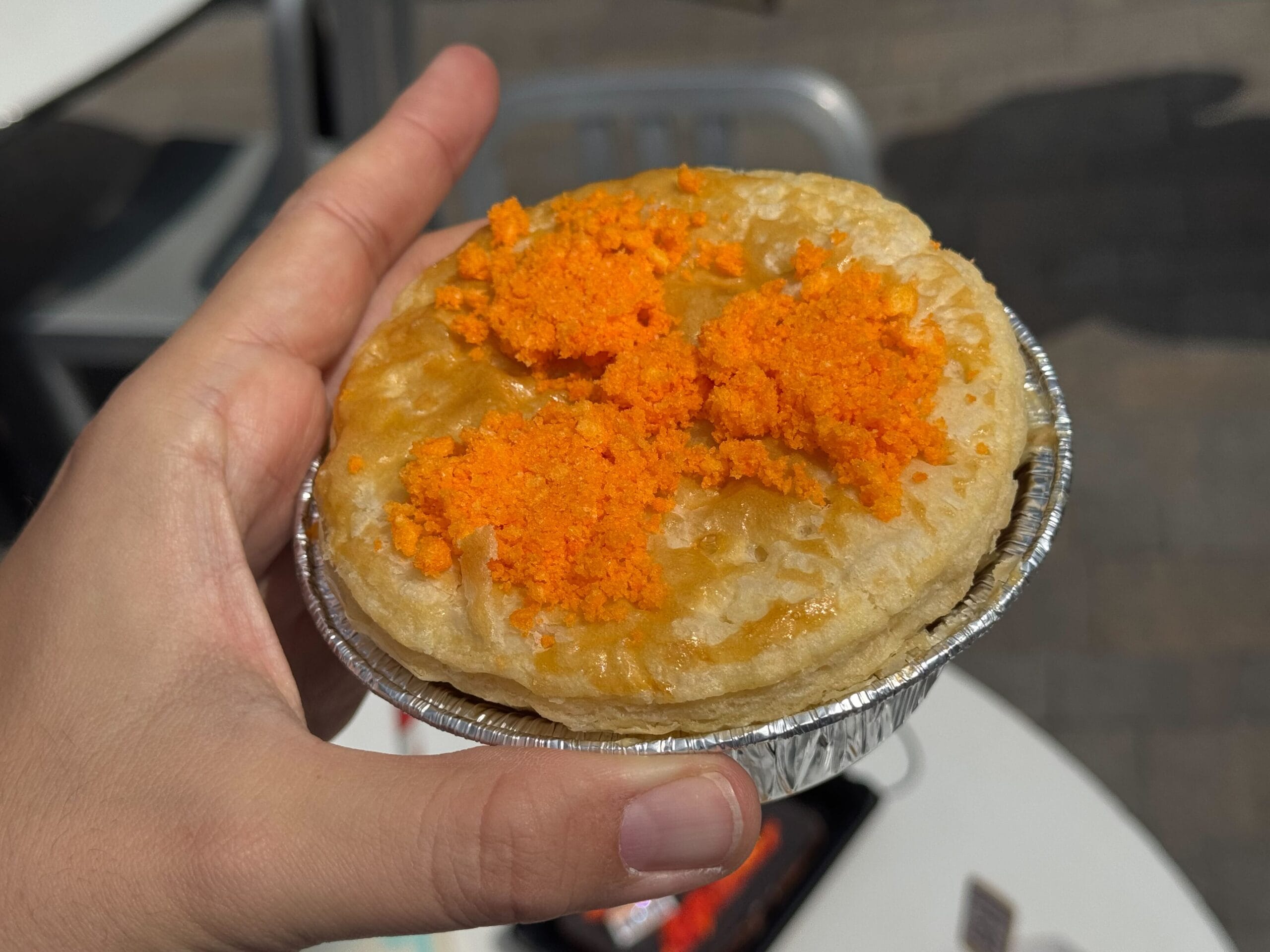 A hand holds a small meat pie topped with bright orange chips—perfect for a quirky Back to the Future food moment.