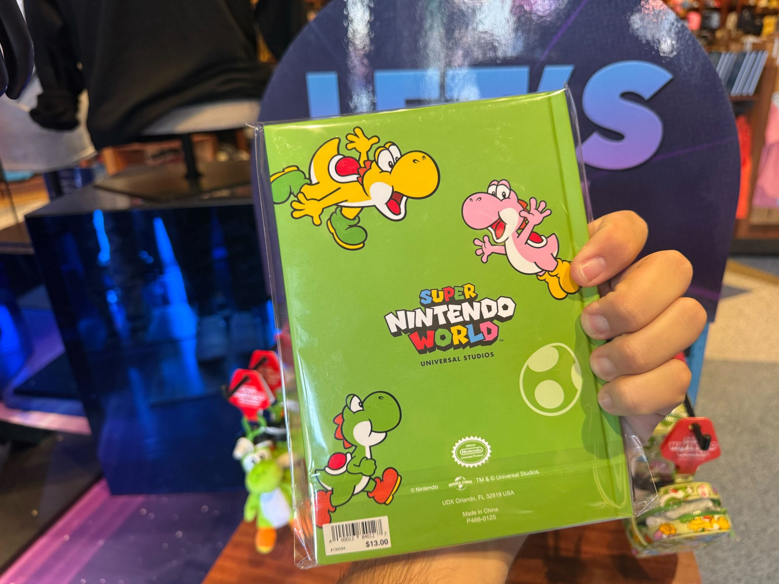 A hand holds Yoshi merchandise—a green Super Nintendo World notebook—at Universal Studios Hollywood.