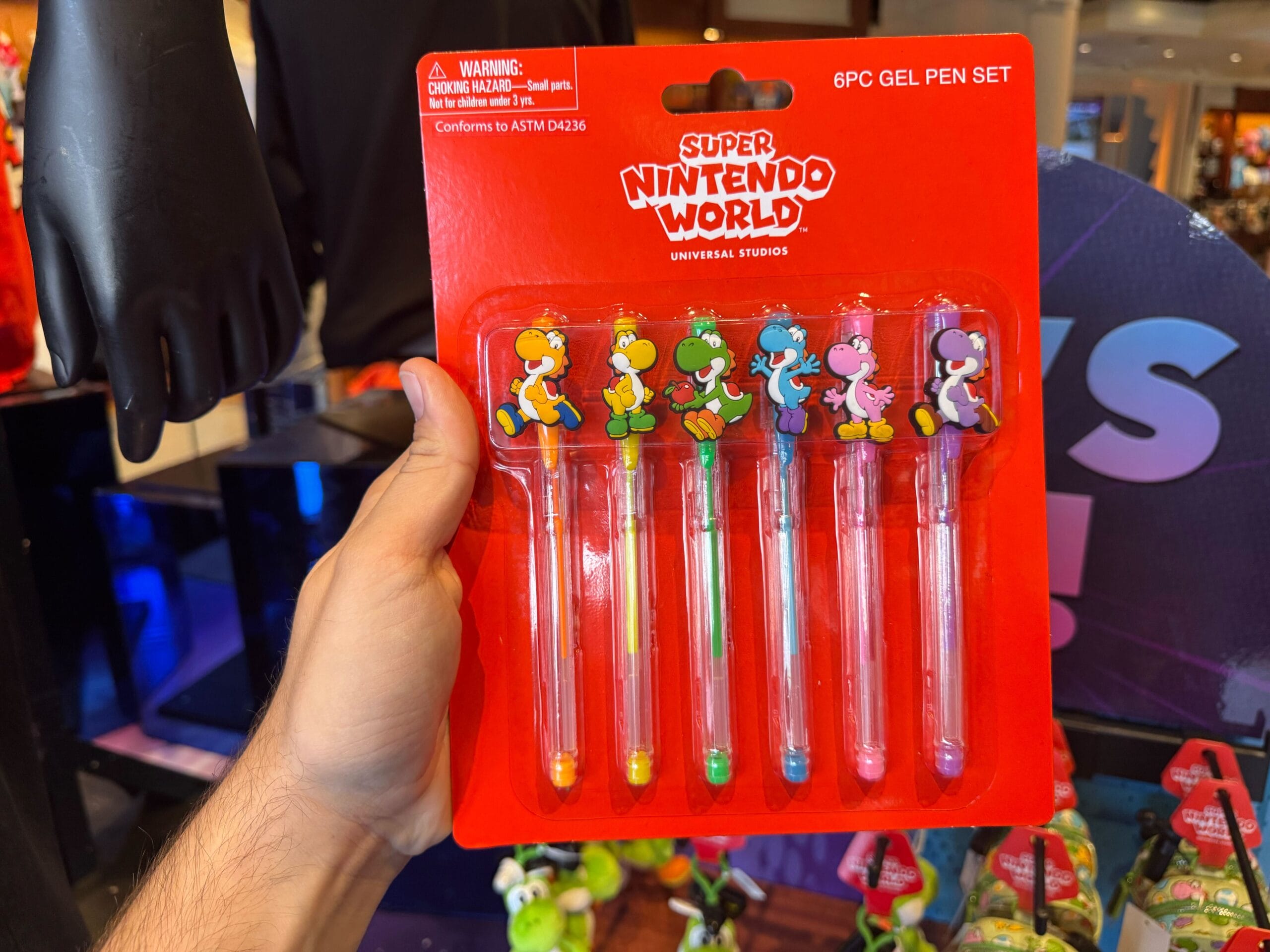 A hand holds Yoshi merchandise: six Super Nintendo World gel pens from Universal Studios Hollywood, each topped with a colorful Yoshi.