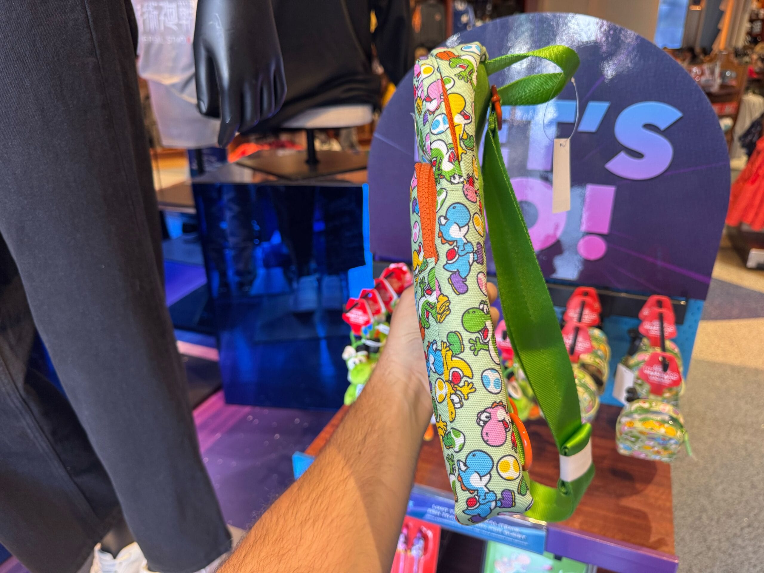 A hand holds colorful Yoshi merchandise in a store at Universal Studios Hollywood, with more bags displayed behind.