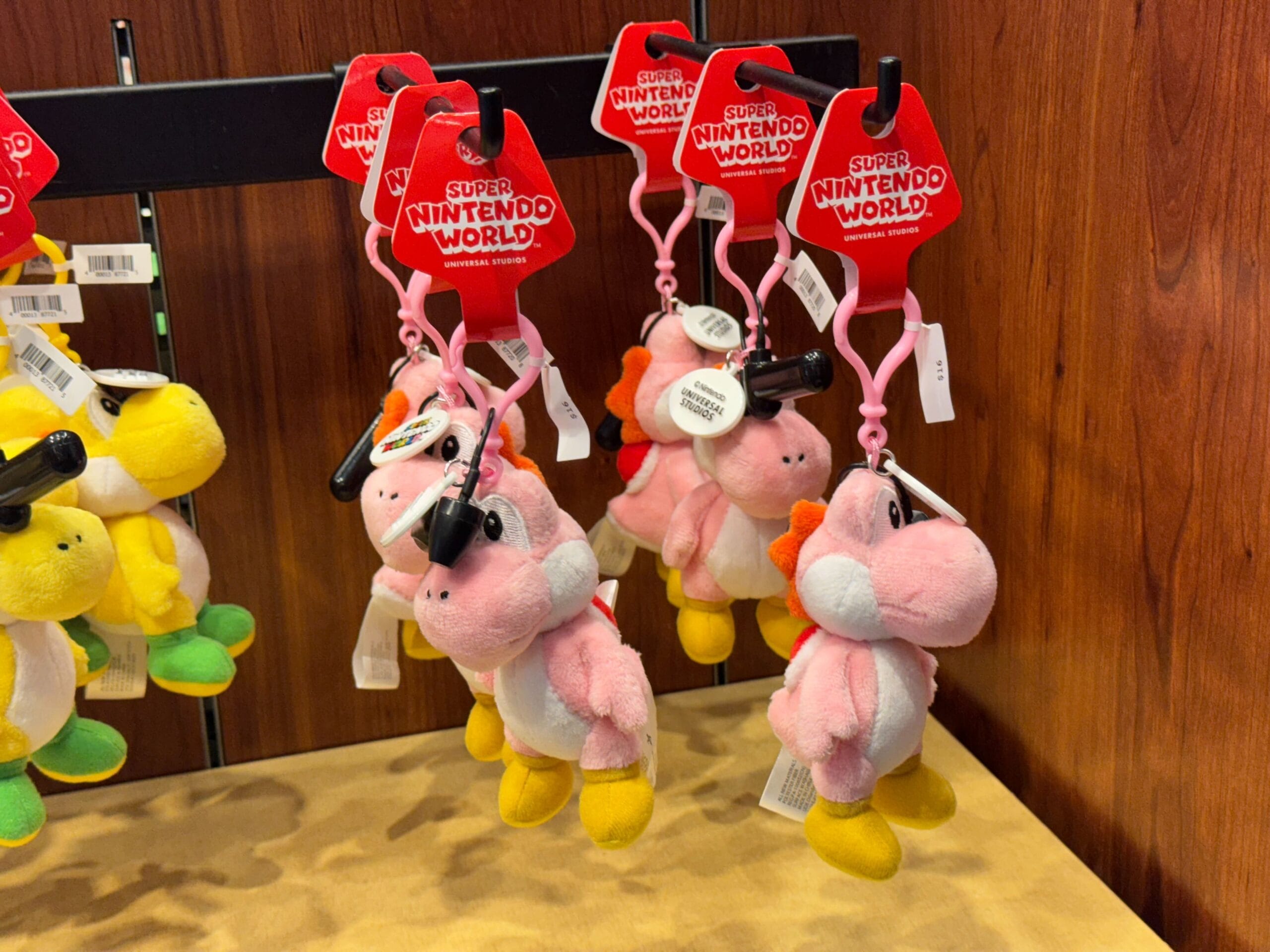 Pink Yoshi plush keychains with Super Nintendo World tags on display at Universal Studios Hollywood.