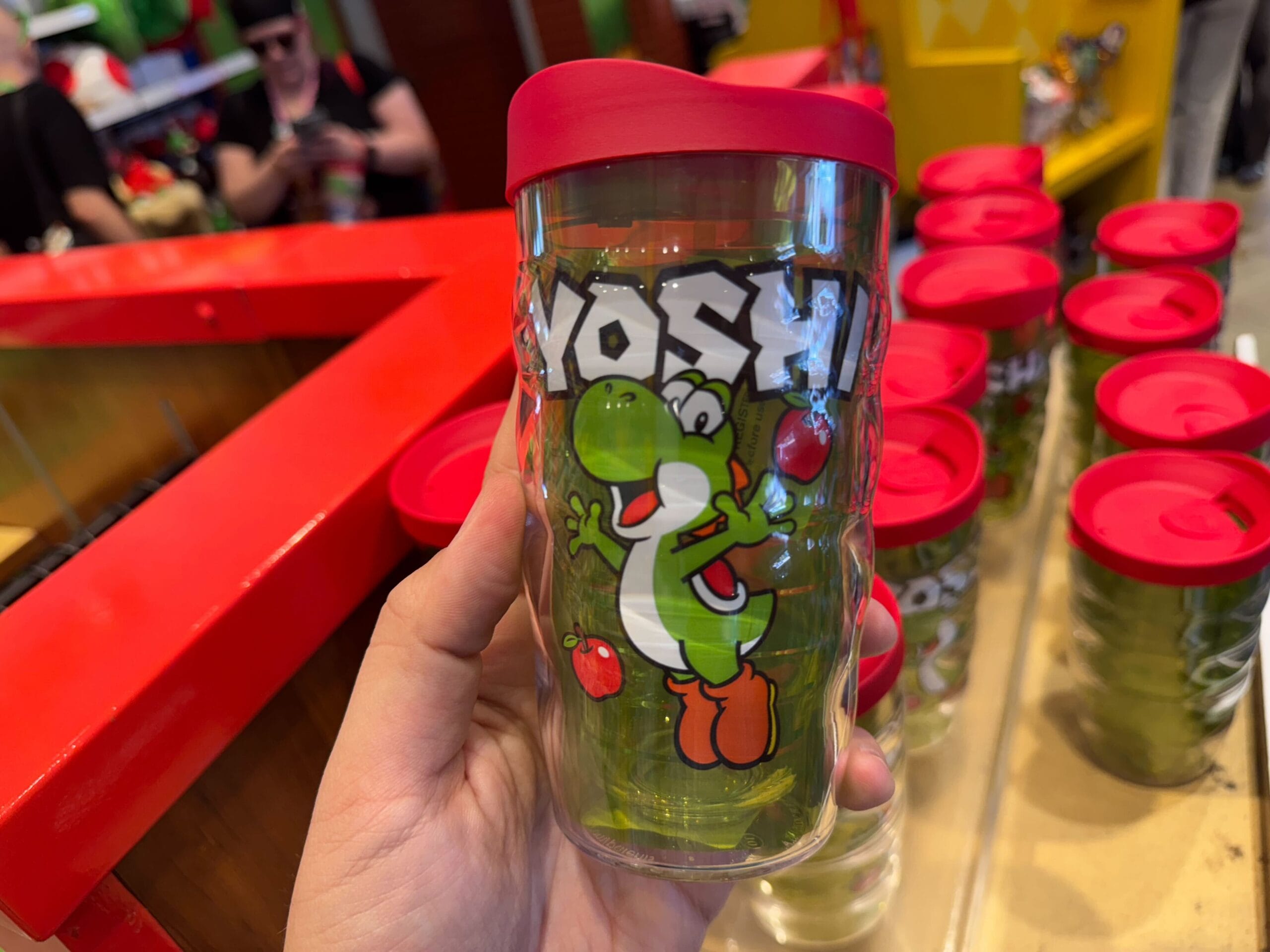 A hand holds Yoshi merchandise—a clear tumbler with red apples—found at Universal Studios Hollywood.