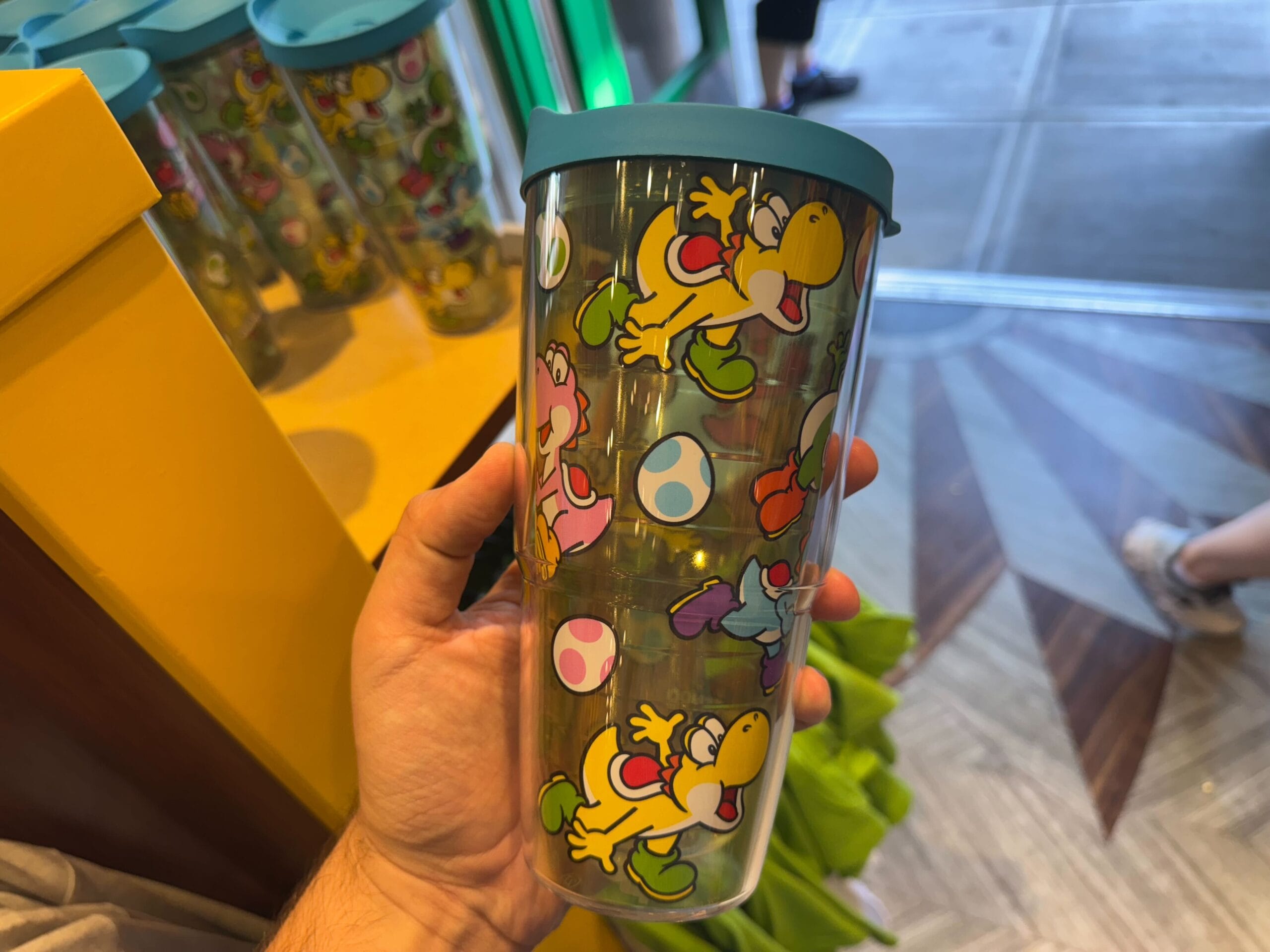 A hand holds Yoshi merchandise—a tumbler with colorful Yoshis and eggs—at Universal Studios Hollywood.