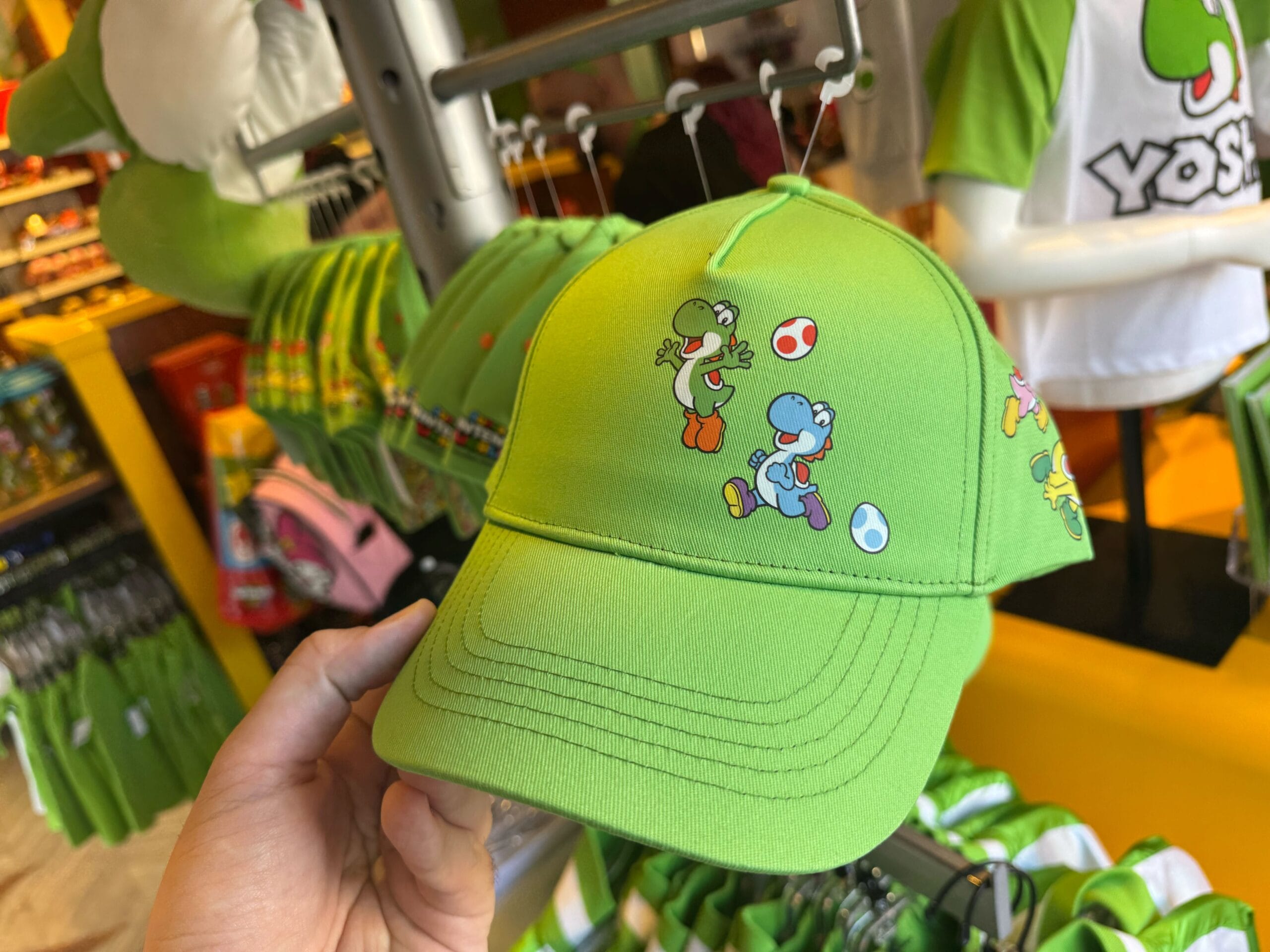 A hand holds a green cap with Yoshi characters among Yoshi merchandise at Universal Studios Hollywood.