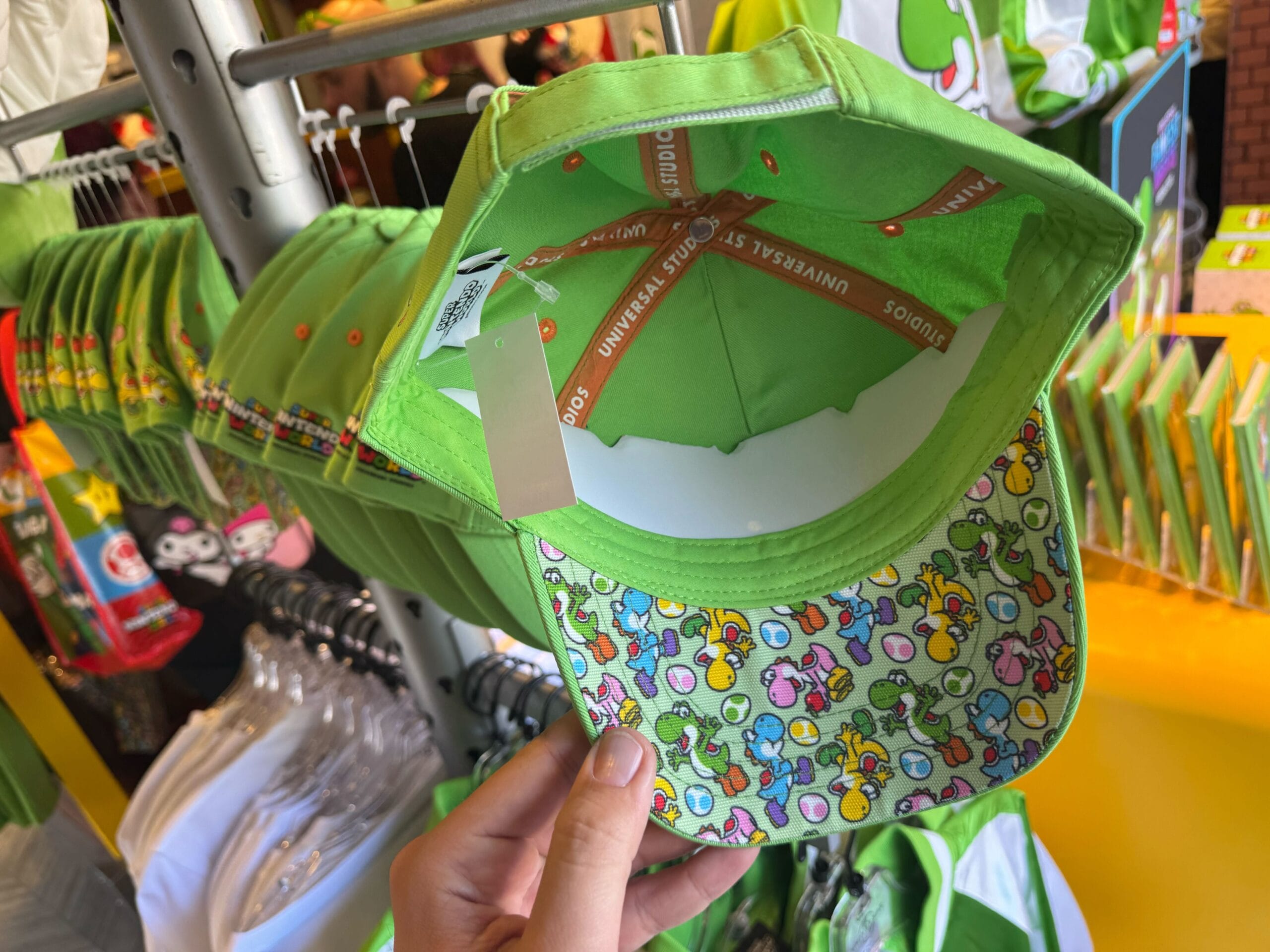 Hand holding a green Yoshi cap—vibrant cartoon pattern under brim—Yoshi merchandise at Universal Studios Hollywood.